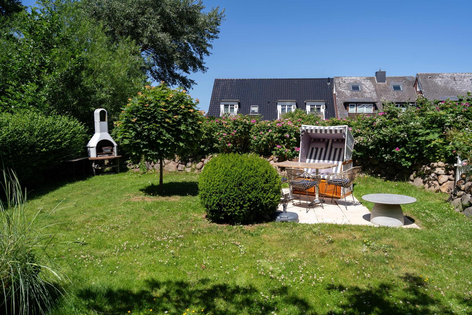 Garten mit Grill, Sitzgruppe und Liege unter blauem Himmel.