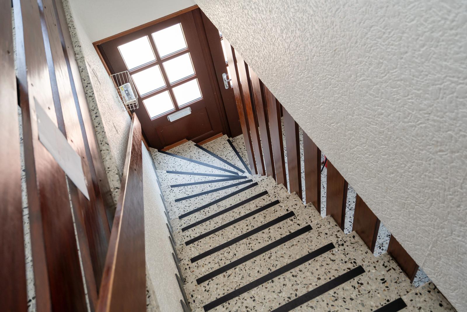 Treppe mit Terrazzoboden und Holzgeländer führt zur Eingangstür.