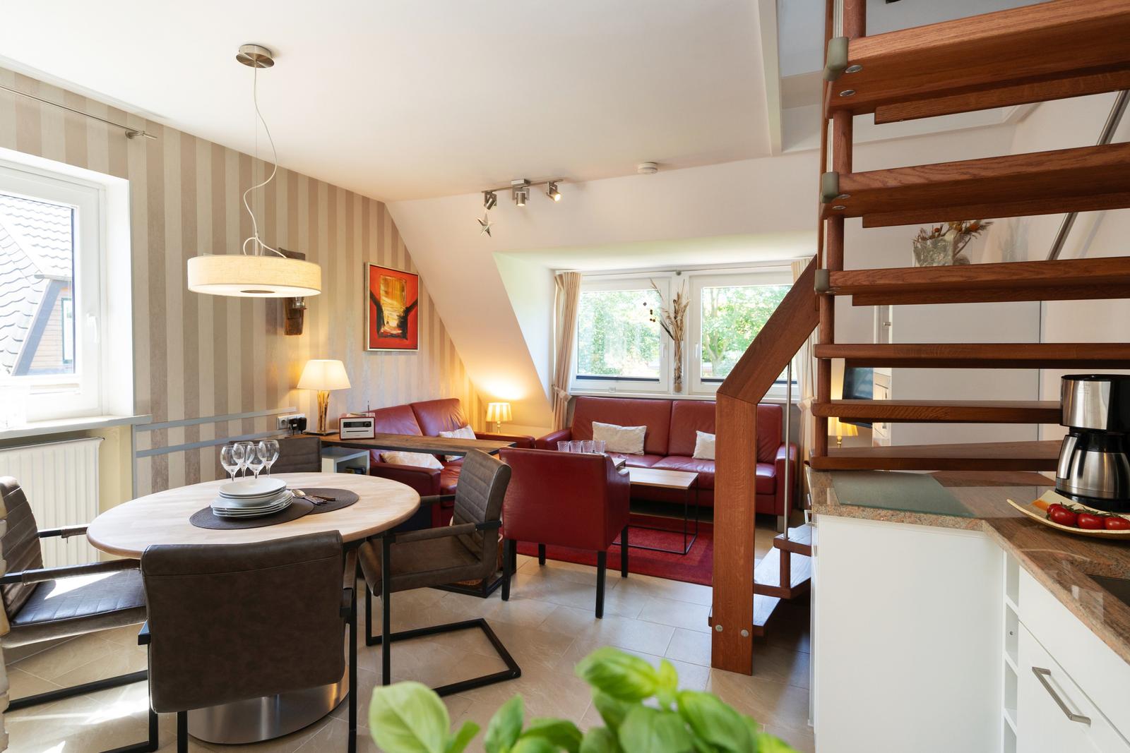 Wohn- und Essbereich mit rotem Sofa, Tisch und Stühlen, Holztreppe und Fenster.