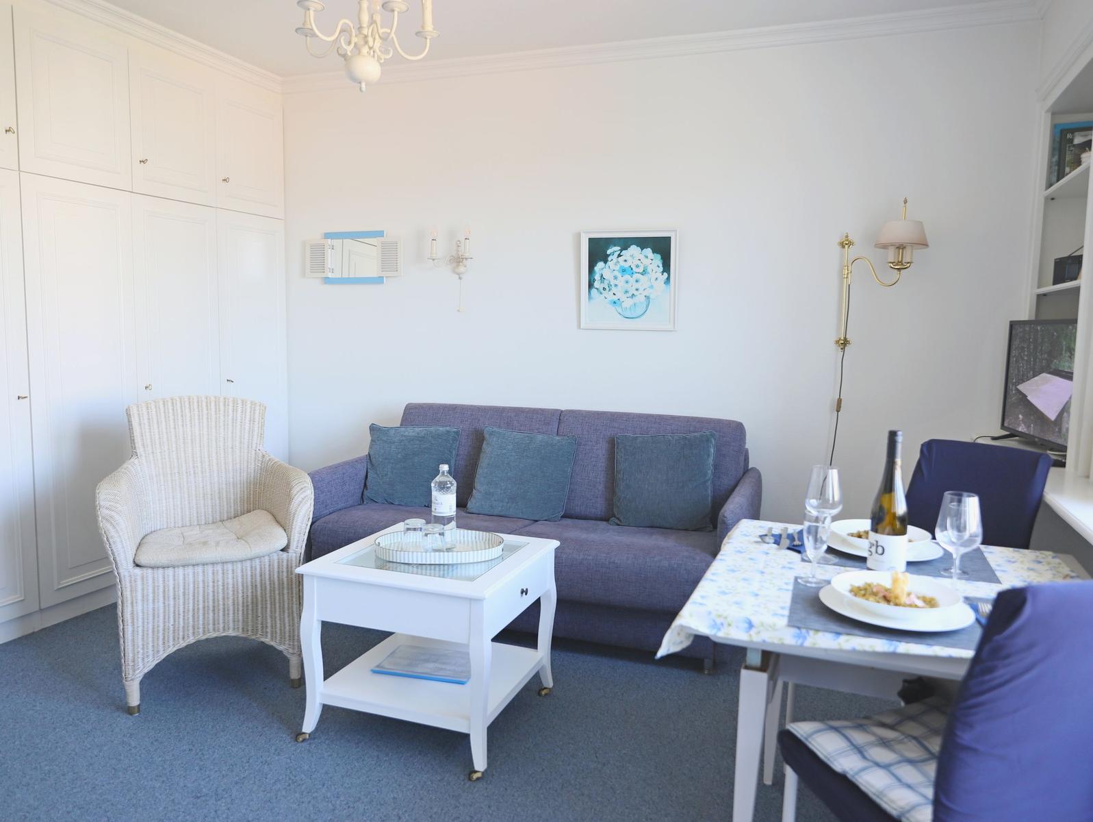 Wohn- und Essbereich mit Sofa, Stuhl und Tisch. Wandbild und Beleuchtung sichtbar.