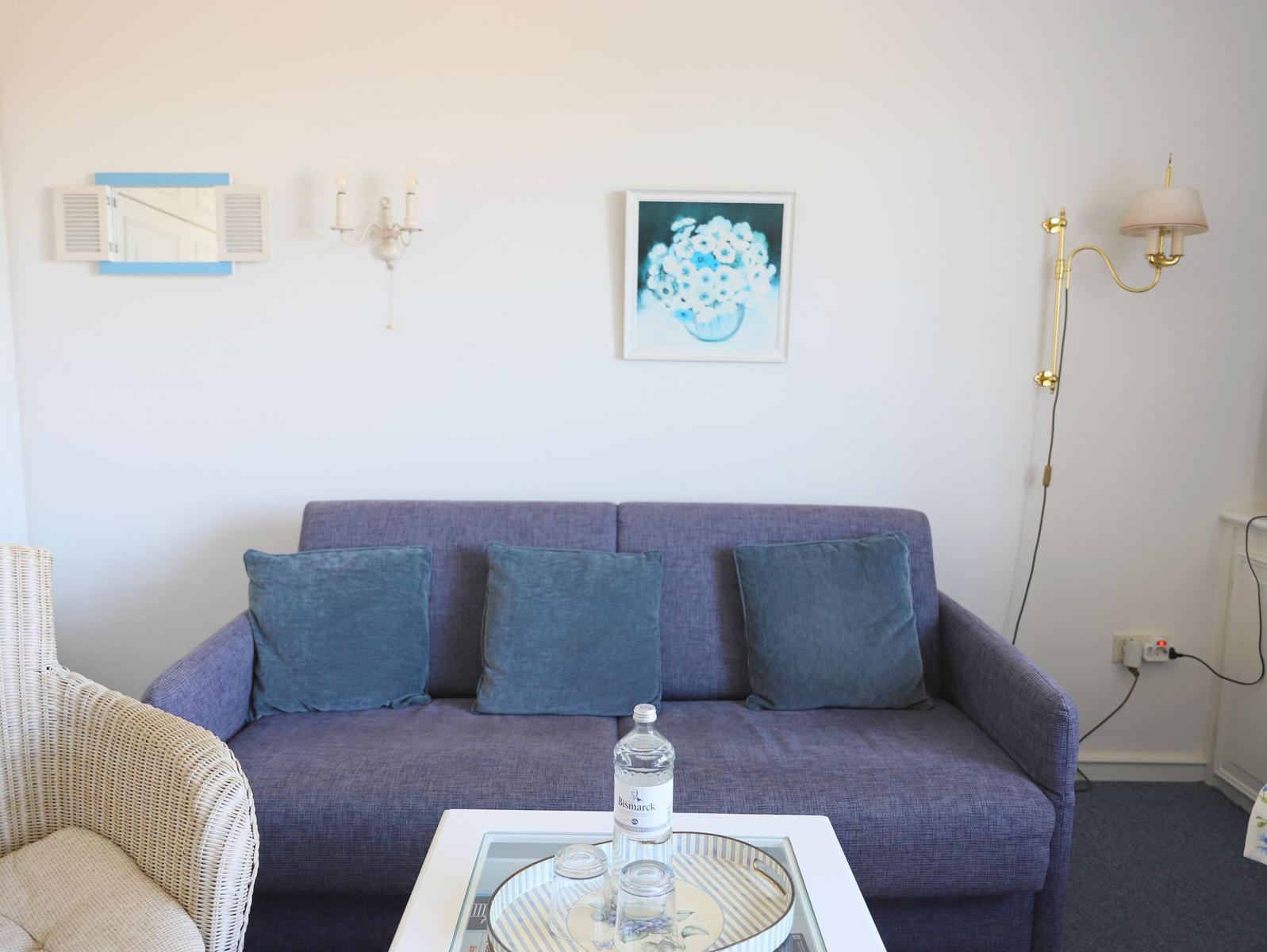 Ein Wohnzimmer mit einem blauen Sofa, einem runden Tisch und einer Wandlampe.