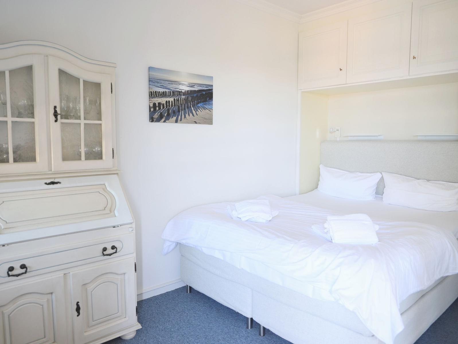Schlafzimmer mit weißem Bett, Schrank und Wandbild