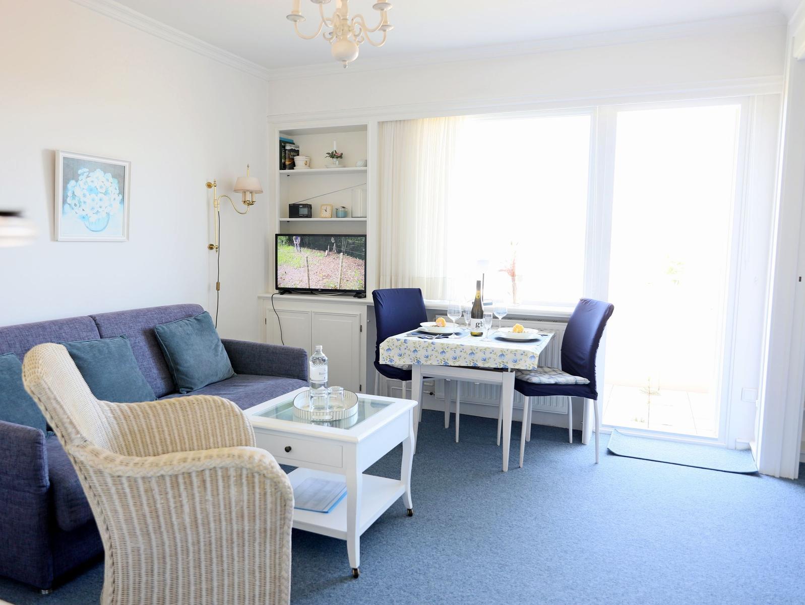 Wohnzimmer mit Sofa, Esstisch und TV. Durchgang zur Terrasse.