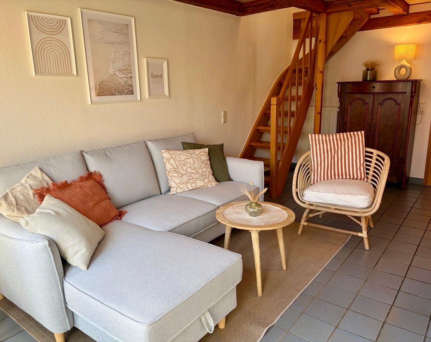 Wohnzimmer mit Sofa, Sessel und Tisch. Holztreppe und Wandbilder sind sichtbar.