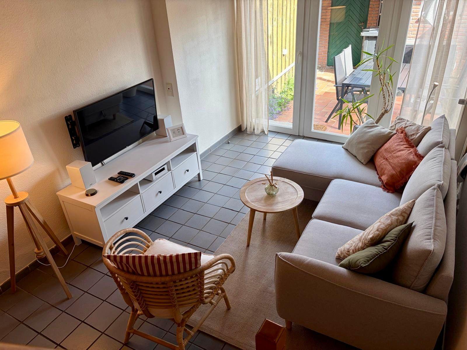 Wohnzimmer mit Sofa, Fernseher und Terrassenzugang.