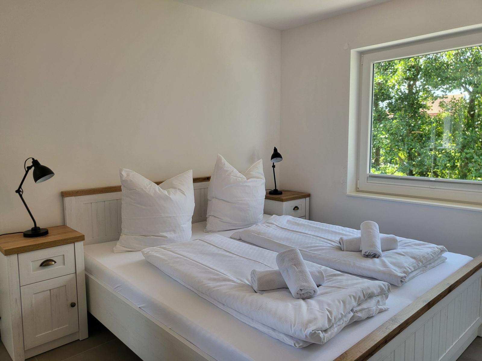 Schlafzimmer mit Doppelbett, zwei Nachttischen und Fensterblick auf Bäume.