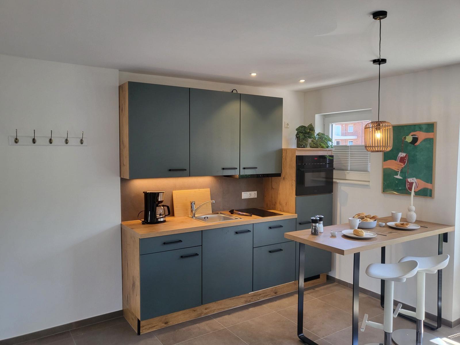 Küche mit Holz Arbeitsplatte, grauen Schränken und Essbereich mit Tisch und Stühlen.