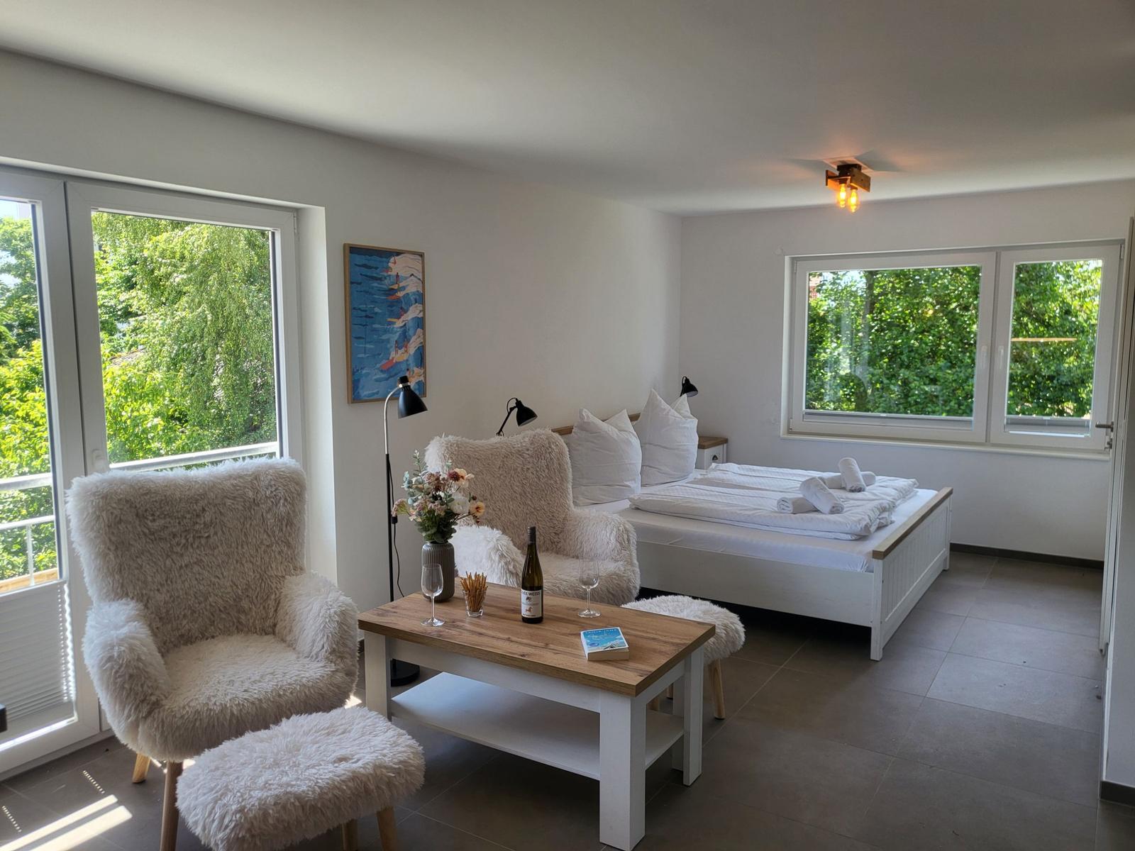 Schlafzimmer mit Bett, Sessel und Tisch. Fenster mit Blick auf Grün.