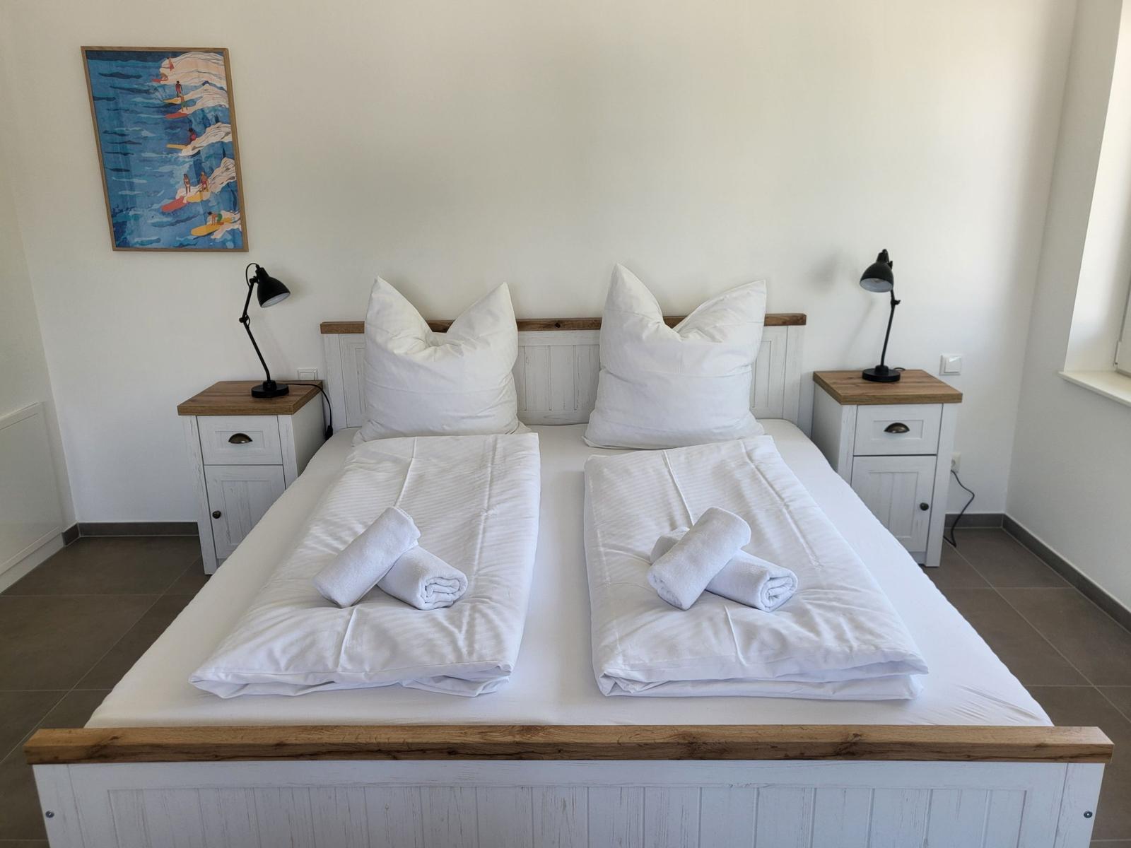 Zimmer mit Doppelbett, zwei Nachttischen und Wandbild.