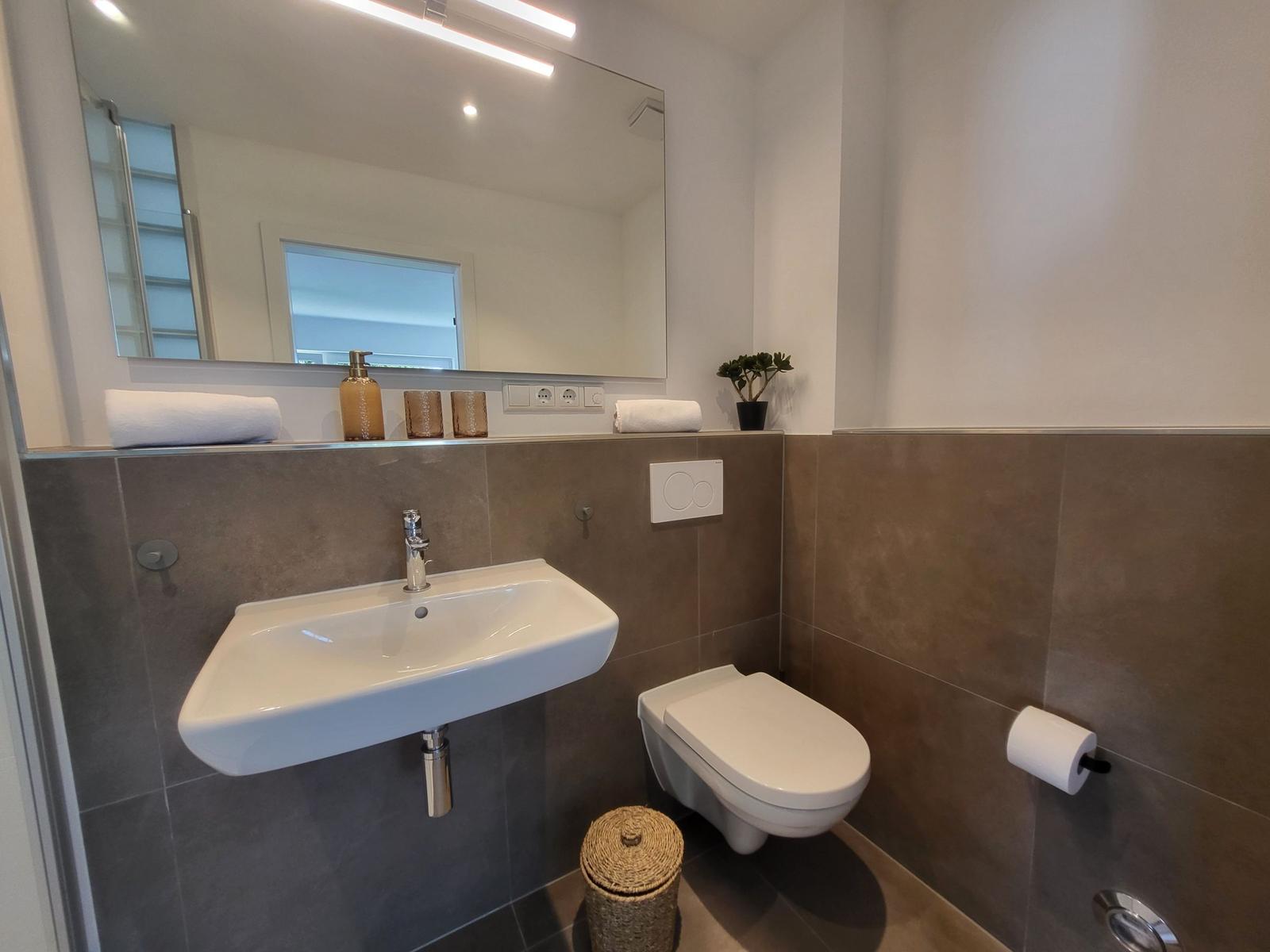 Badezimmer mit Waschbecken, Toilette und Spiegel. Wandfliesen und Handtuch.