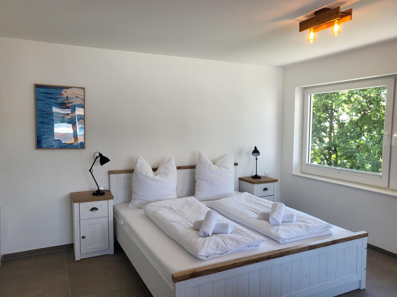 Schlafzimmer mit Doppelbett, zwei Nachttischen und Fenster mit Blick auf Bäume.