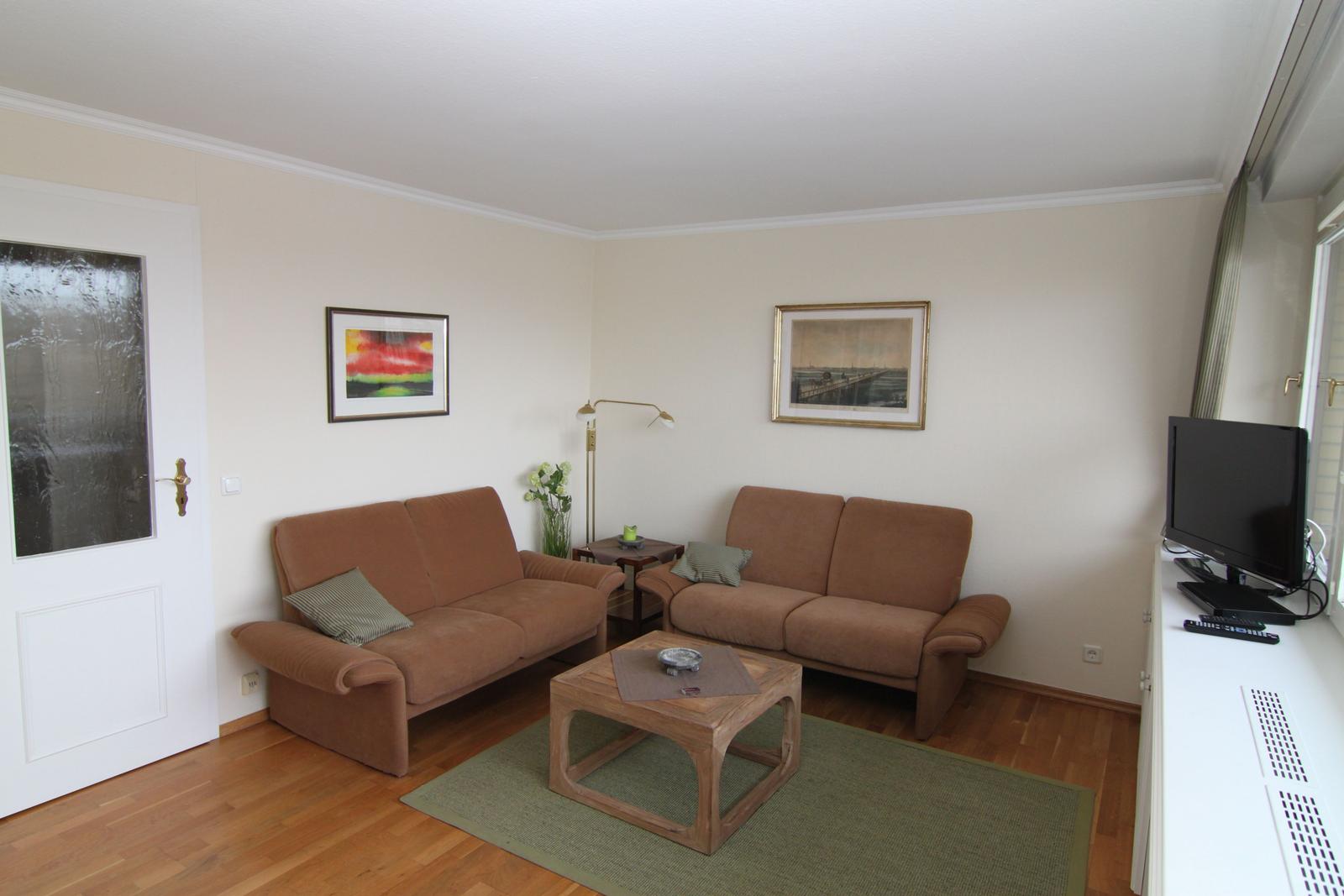 Wohnzimmer mit zwei braunen Sofas, Holztisch, Fernseher und Wandbildern.