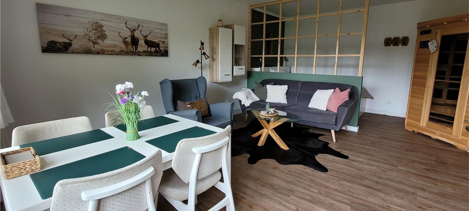Essbereich mit Tisch und Stühlen, Wohnbereich mit Sofa und Sessel, Holzfußboden und Sauna.