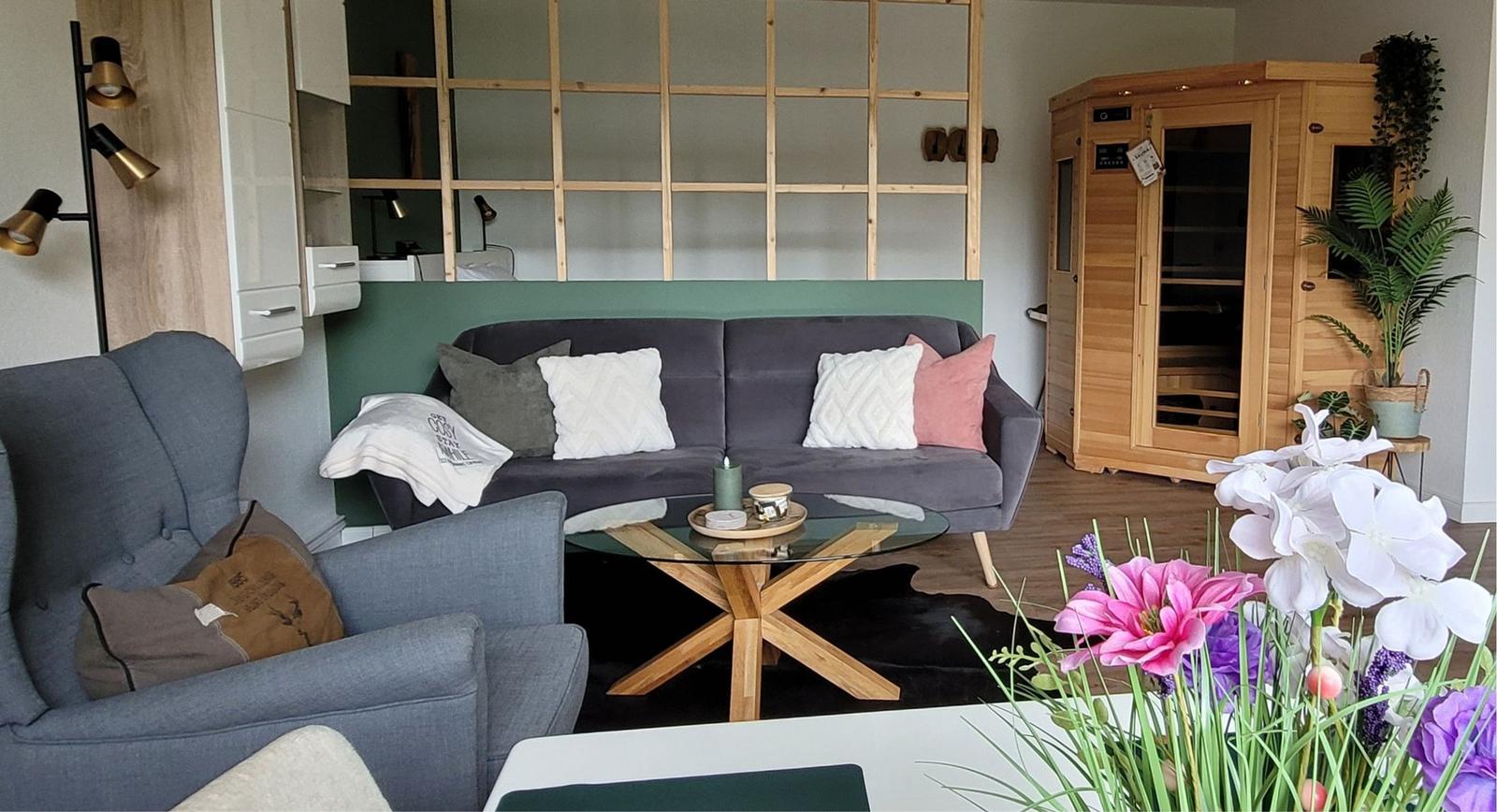 Wohnzimmer mit Sofa, Sessel, Glas-Tisch und Holzsauna