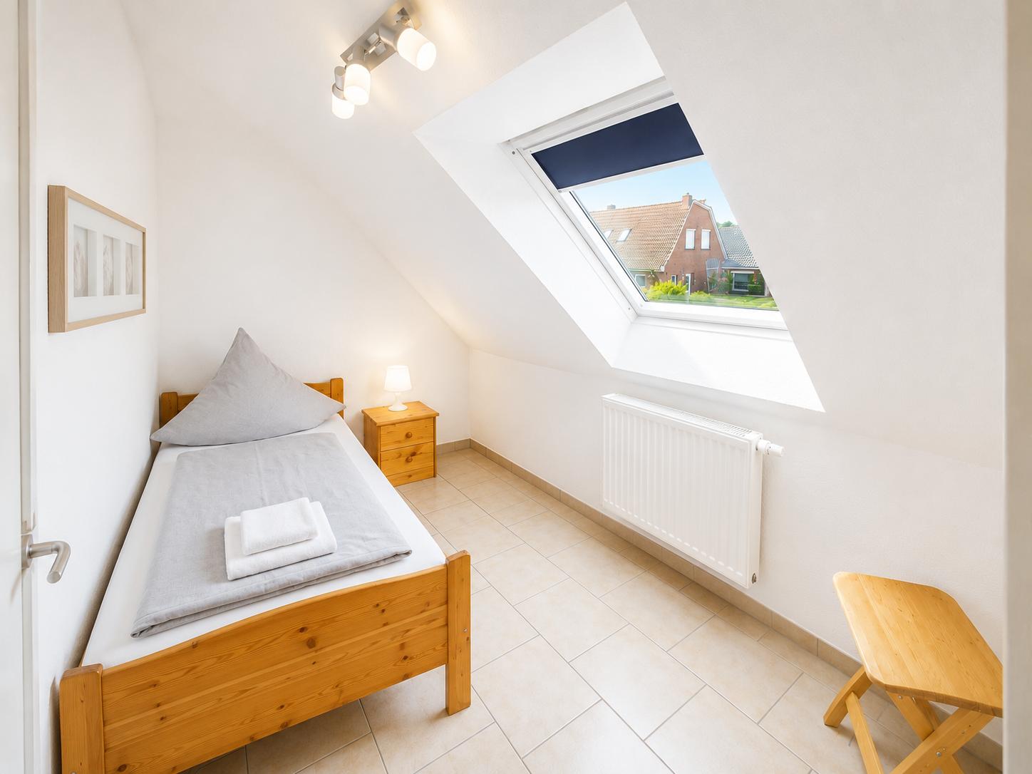 Ein Schlafzimmer mit Dachfenster, Bett, Nachttisch und Stuhl.
