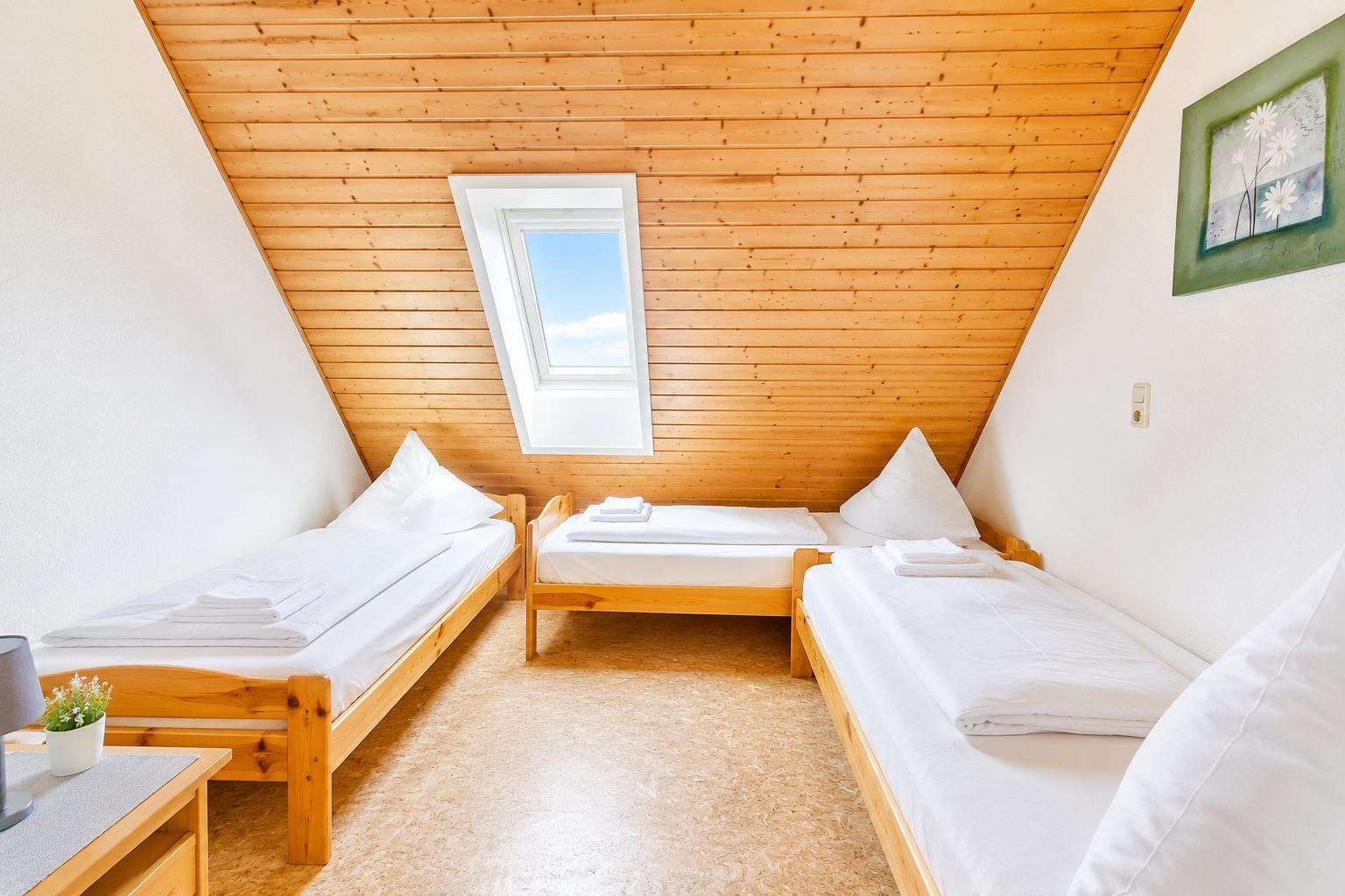 Dreibettzimmer mit Holzdach, Dachfenster und weißen Bettwäschen.