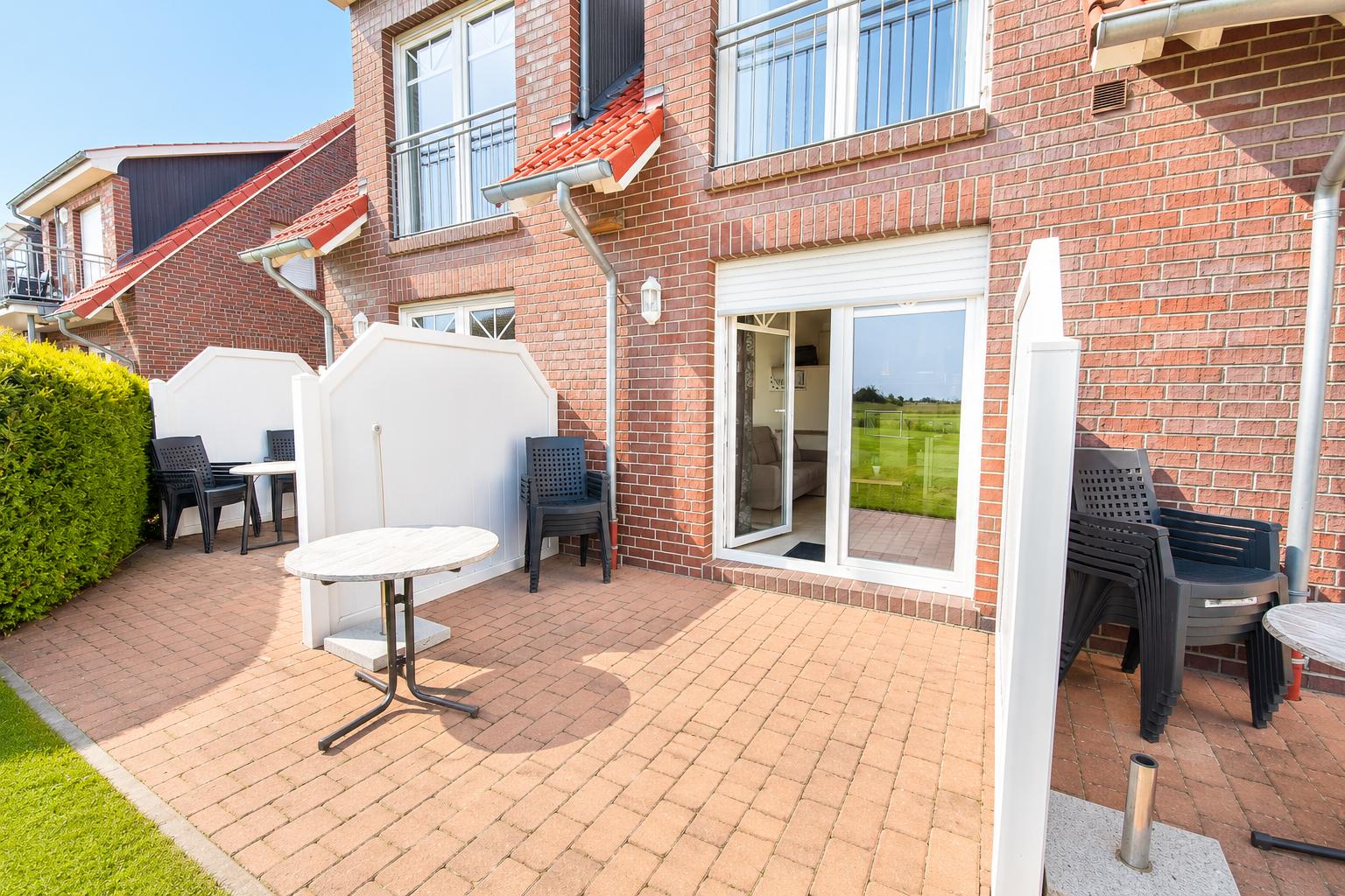 Terrasse mit Tischen und Stühlen vor einem Haus mit rotem Ziegelmauerwerk und Glasfront.
