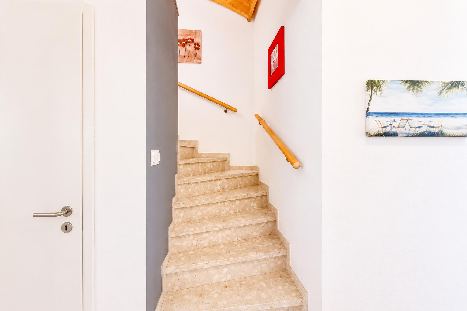 Treppenhaus mit Holzgeländer und Terrazzo-Stufen. Wandbilder zeigen Strand und Blumen.