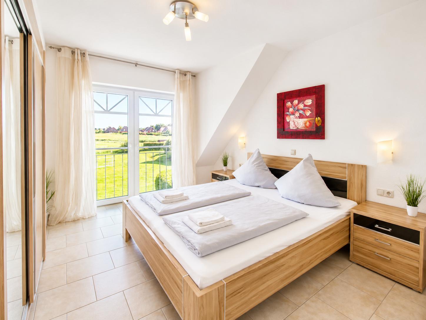 Schlafzimmer mit Doppelbett, Fenster zum Garten und Wandbild.