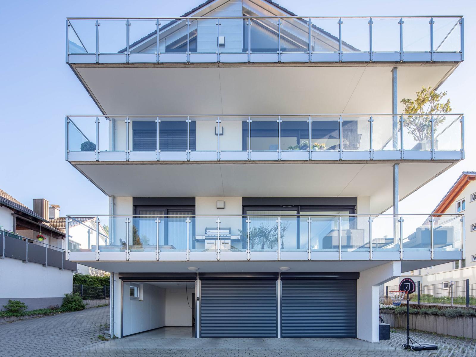 Moderne Villa mit drei Balkonen und Garage. Glasgeländer und großzügige Fenster.