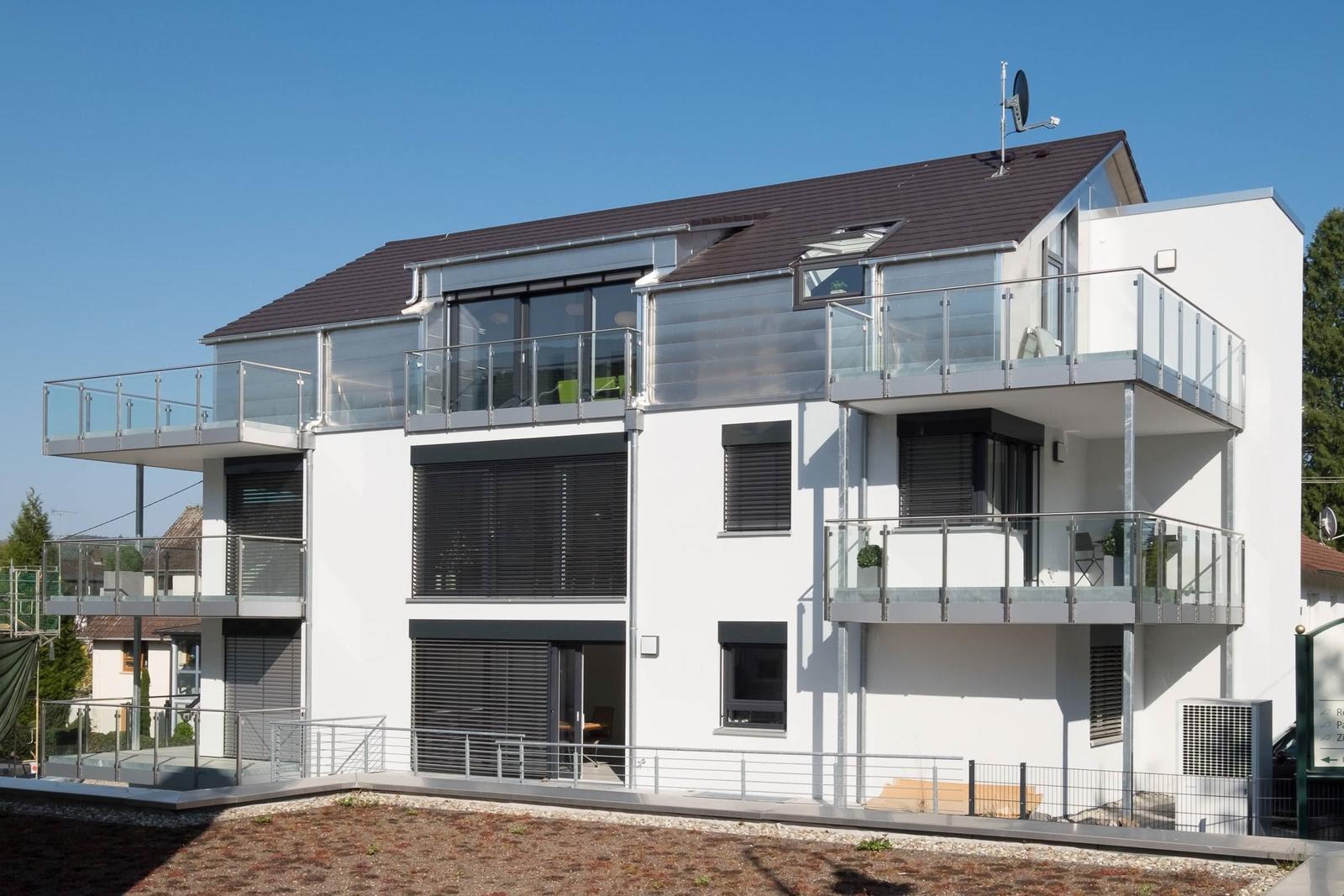 Moderne weiße Villa mit Balkonen und großen Fenstern. Dachterrasse mit Sichtschutz.