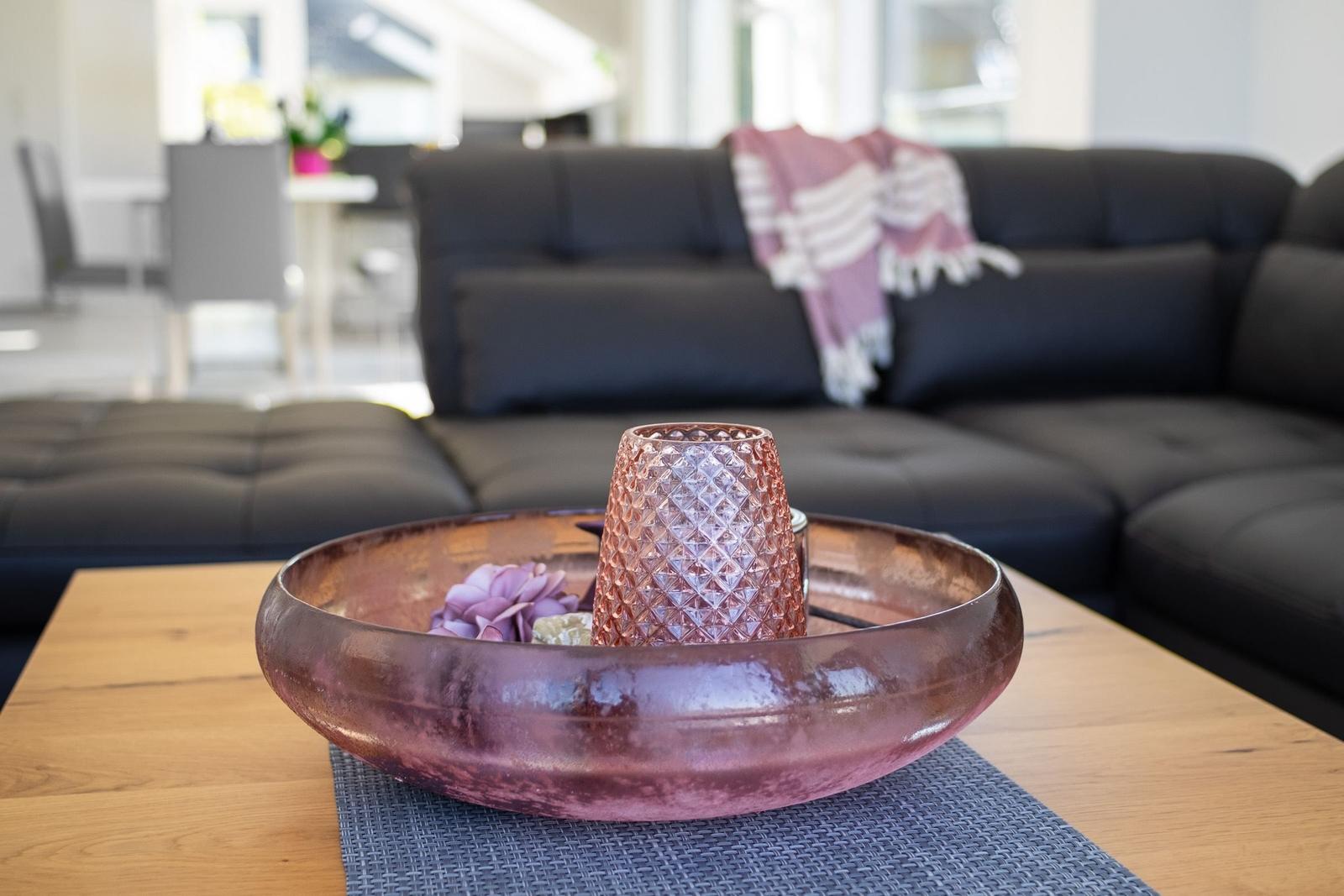 Ein dunkler Sofa im Hintergrund. Auf dem Tisch steht eine rosa Schale mit Deko.