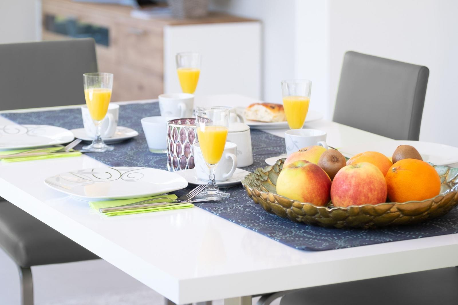 Tisch mit Frühstück, Obstschale und Gläsern mit Saft.