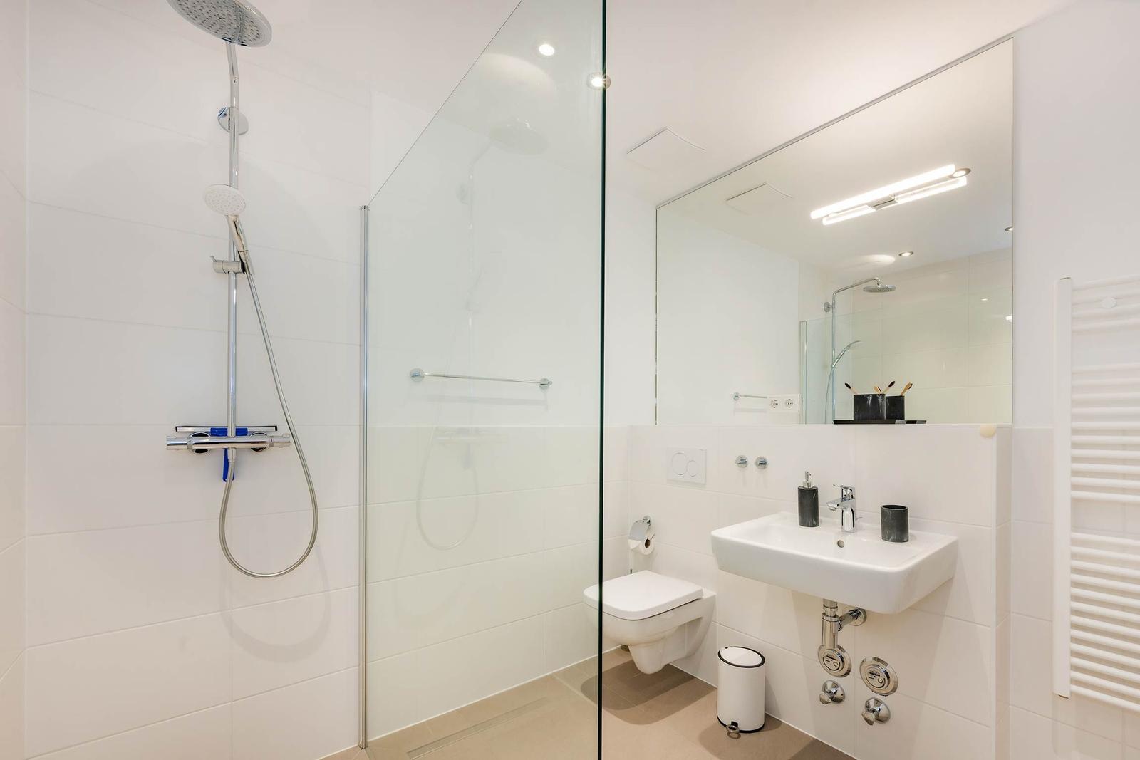Dusche mit Glaswand, Waschbecken und Toilette in weißer Ausstattung.