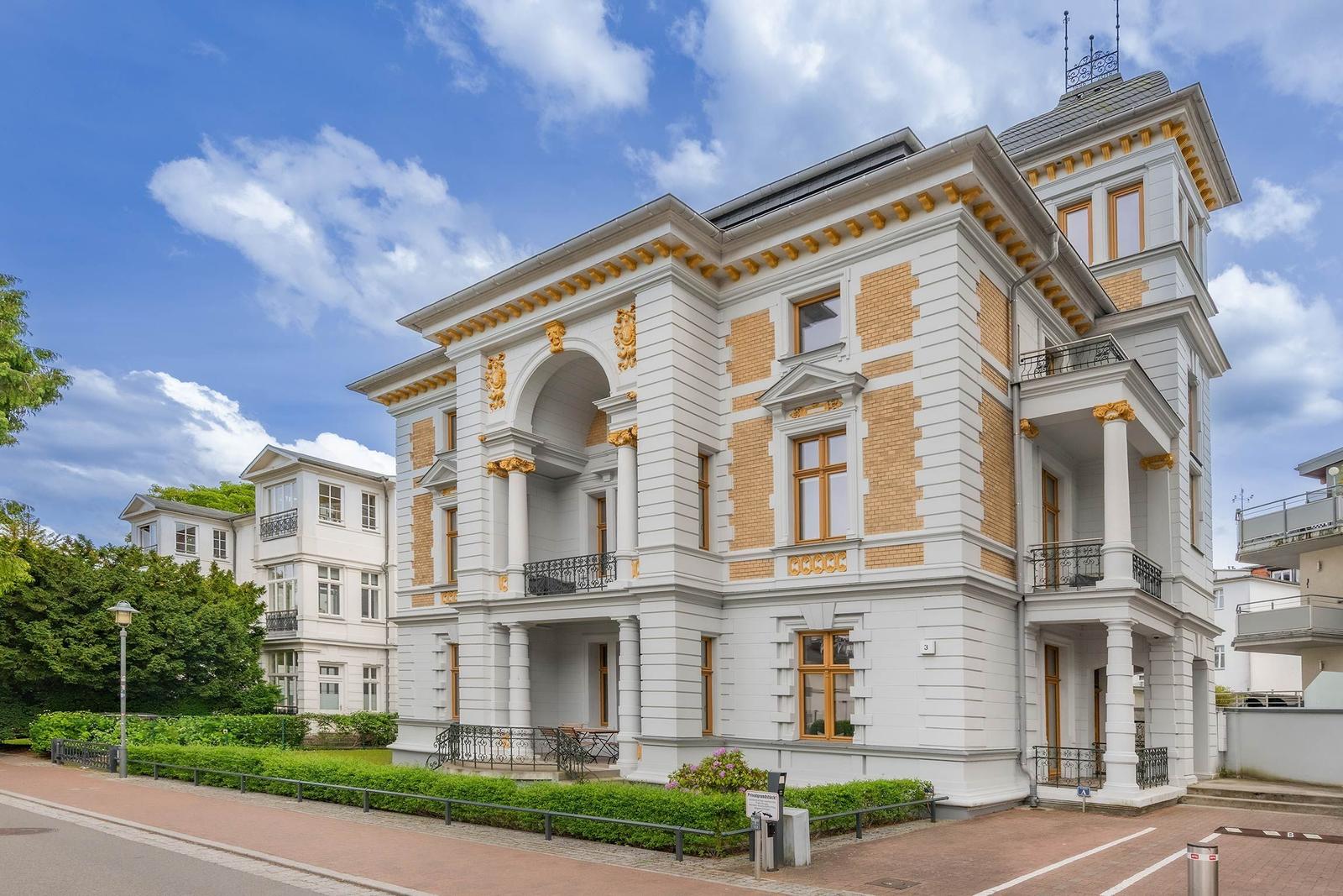 Historisches Gebäude mit Balkonen und goldenen Verzierungen unter blauem Himmel.