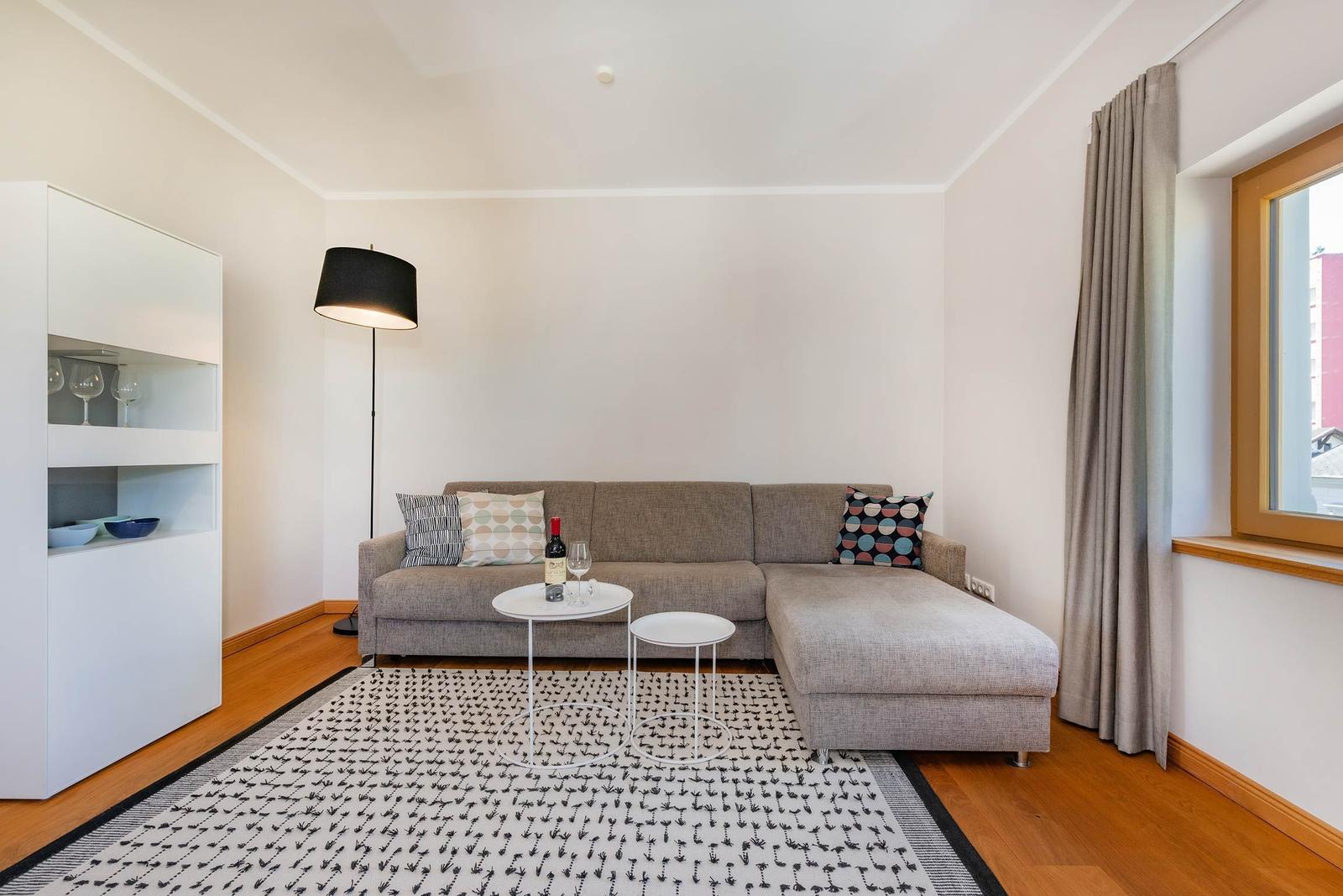 Wohnzimmer mit grauem Sofa, weißen Tischen und Holzboden.