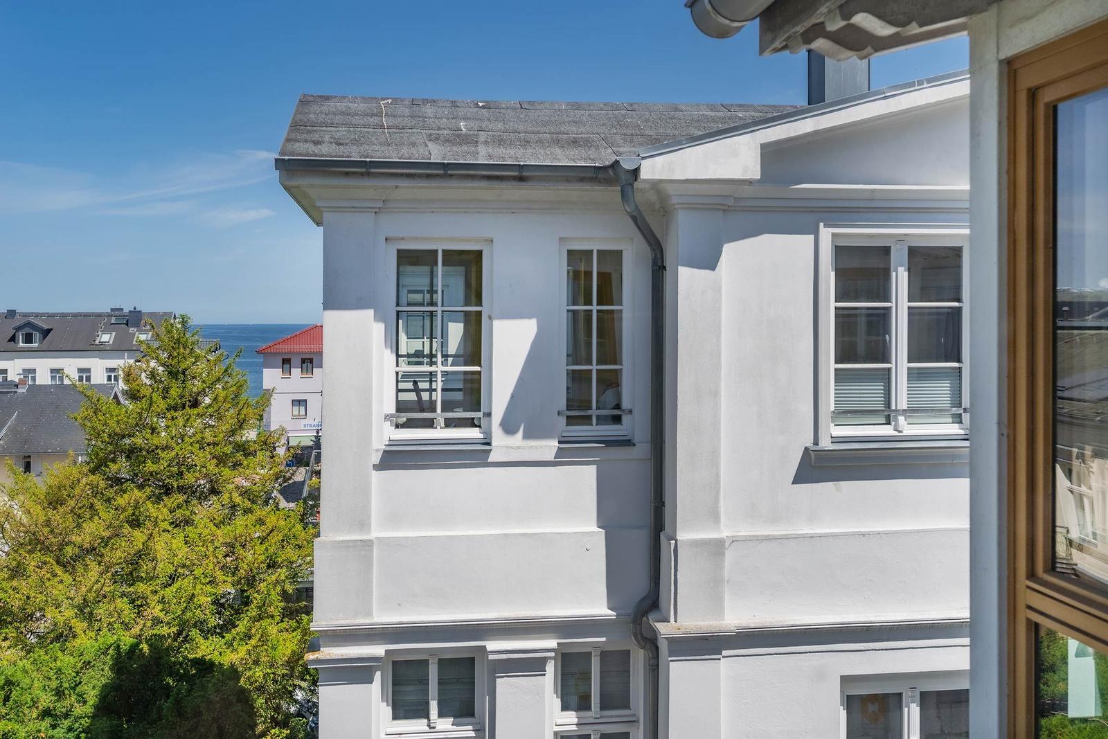 Weißes Gebäude mit Fenstern und Blick auf Meer und Bäume.