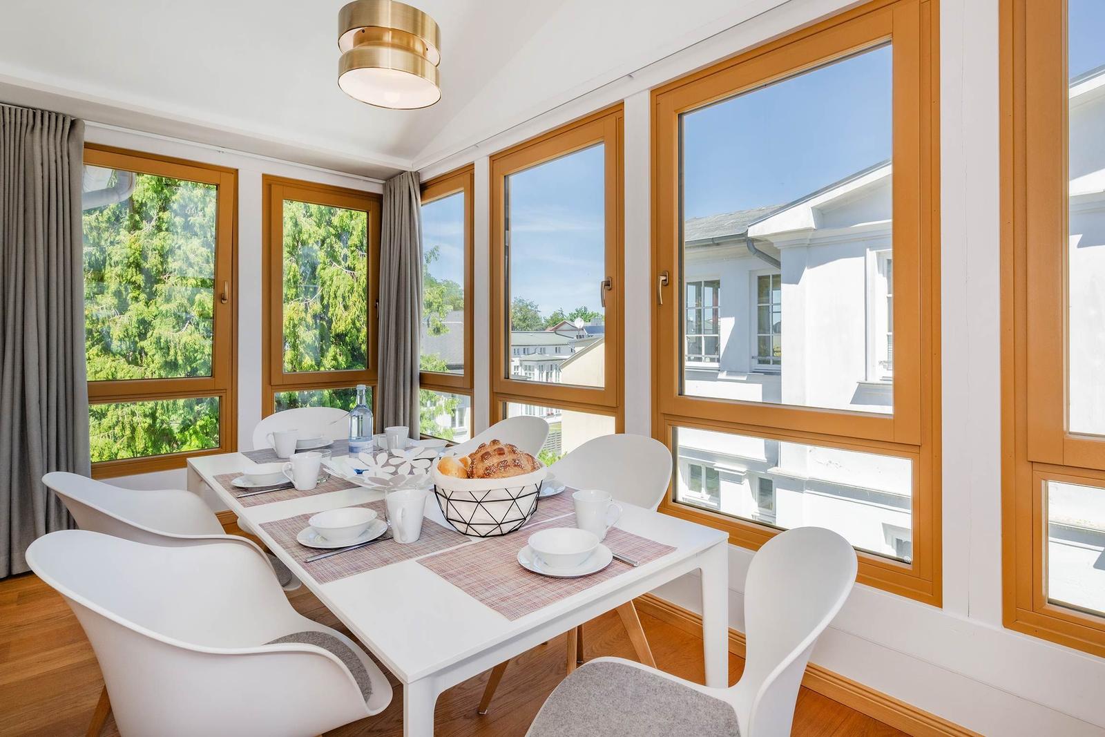 Esszimmer mit weißem Tisch, Stühlen und Fenstern zum Blick auf Grün und Gebäude.