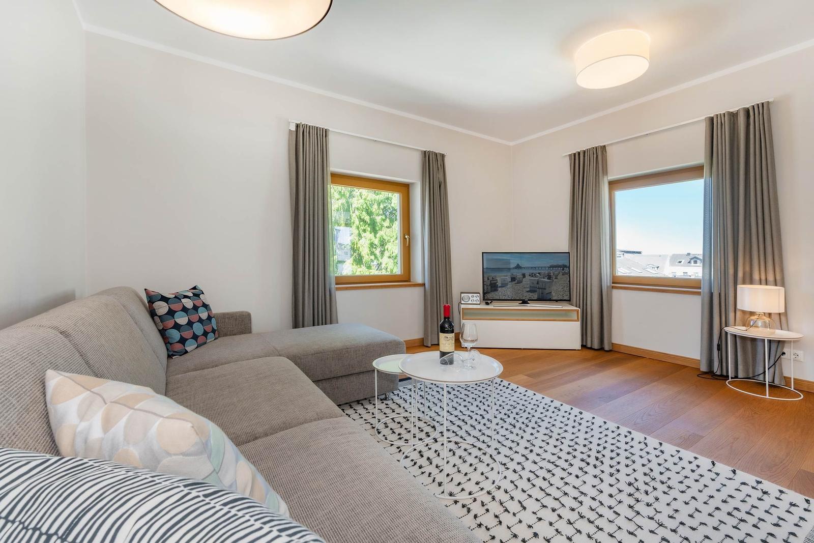 Wohnzimmer mit Sofa, Fernseher und zwei Fenstern mit Blick.