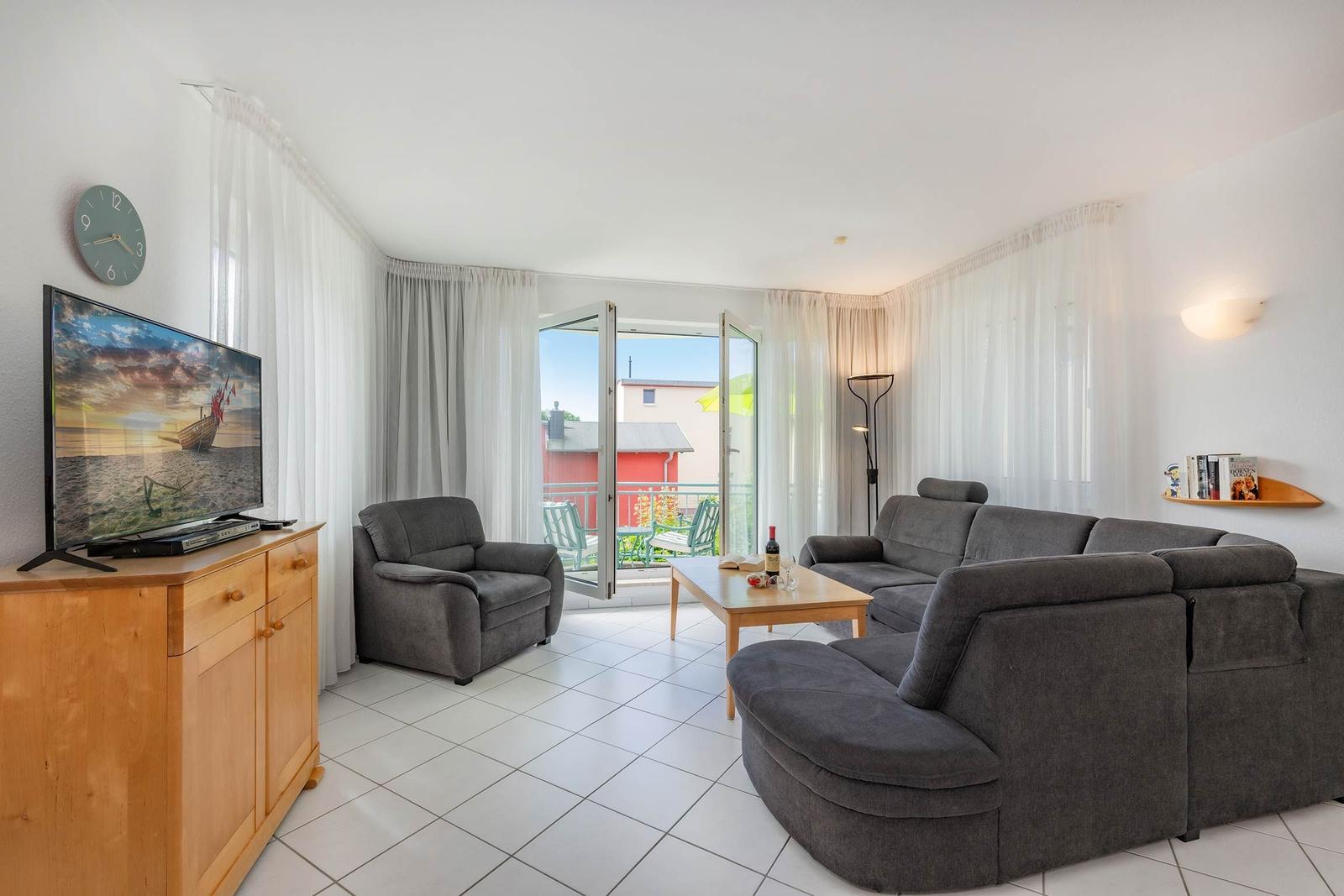 Wohnzimmer mit Sofa, Sessel, TV und Balkonzugang.