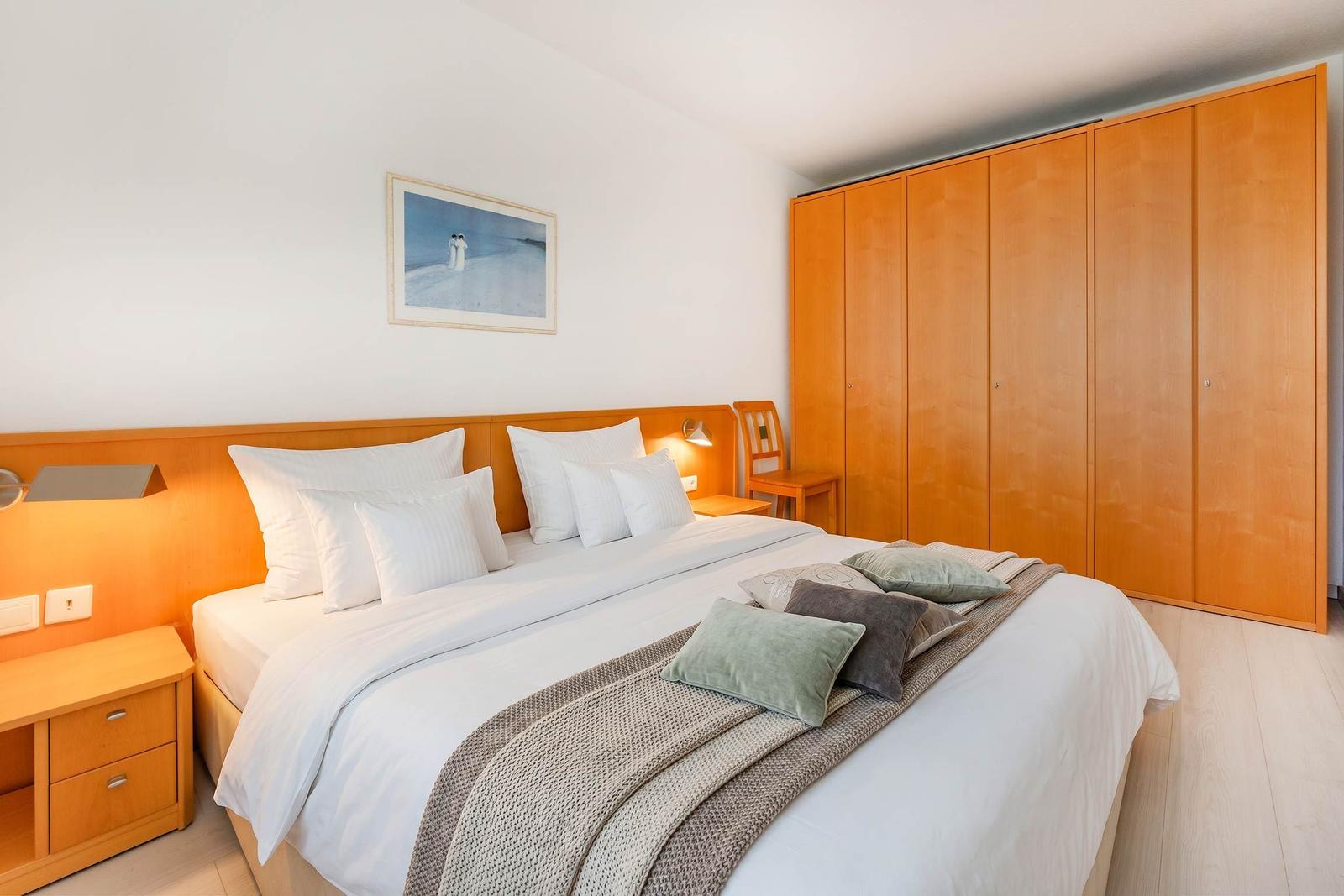 Schlafzimmer mit Doppelbett, Holzschrank und Nachttisch. Wandbild über dem Bett.