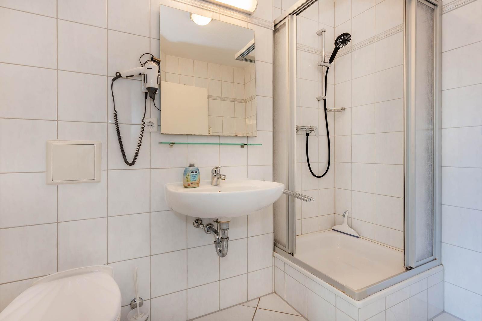 Badezimmer mit Dusche, Waschbecken und Toilette. Wandtrockner und Spiegel sind vorhanden.