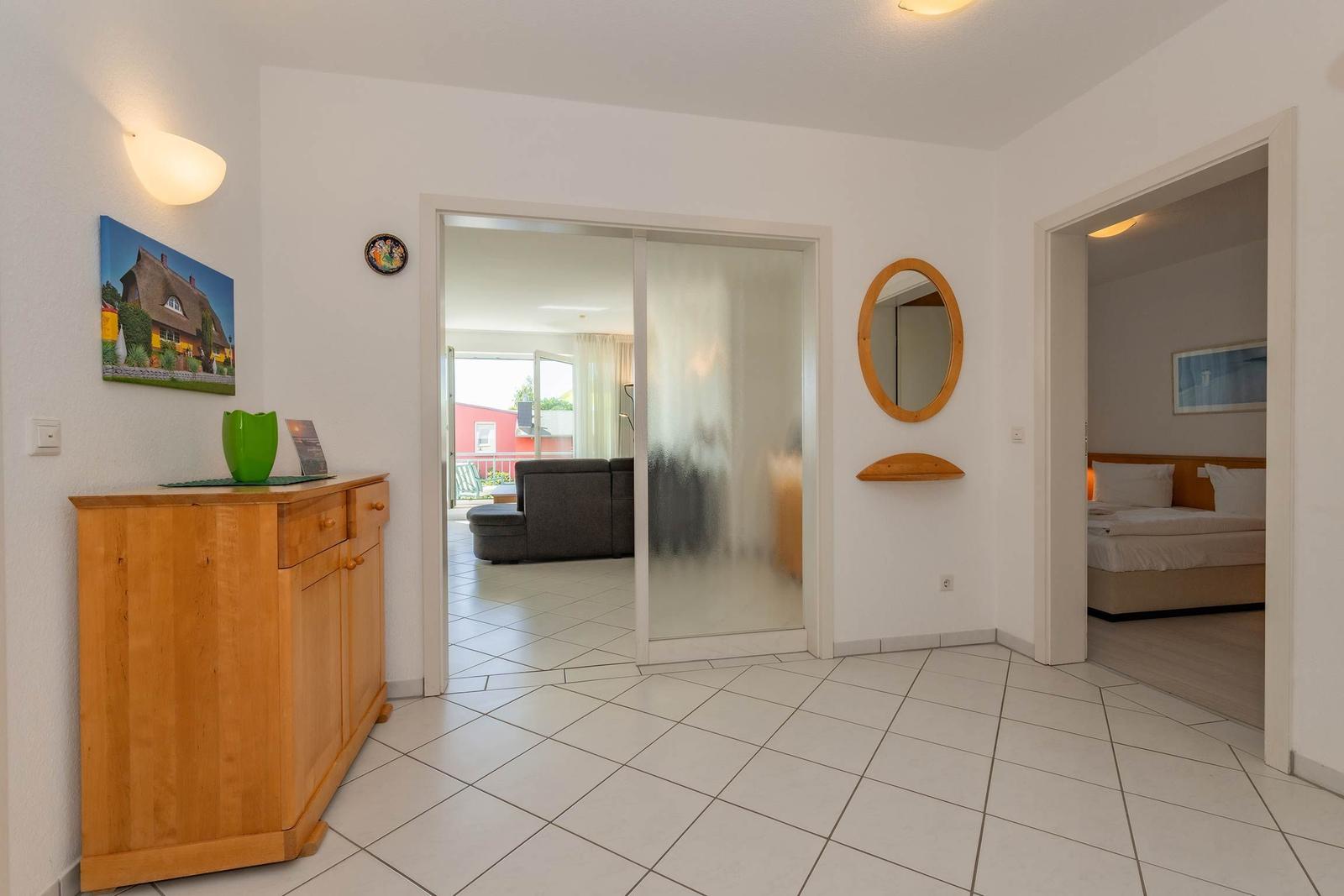 Eingangsbereich mit Holzschrank, Spiegel und Blick in Wohn- und Schlafzimmer.