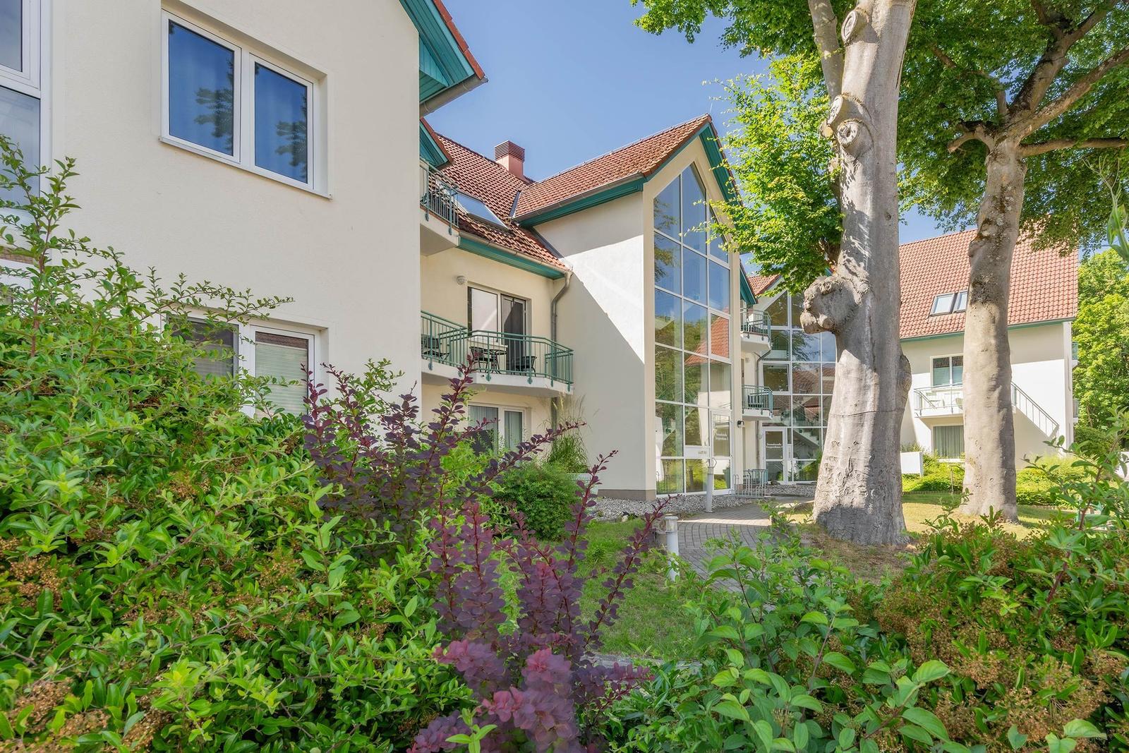 Haus mit Balkon, großen Fenstern und grüner Umgebung