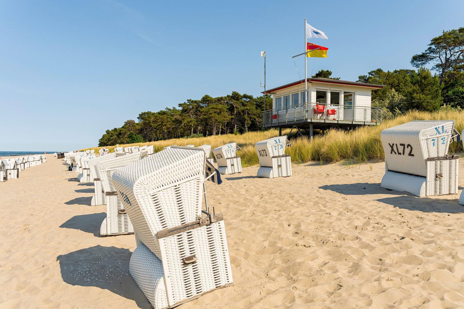 Strand mit weißen Liegestühlen und Strandhaus im Hintergrund.