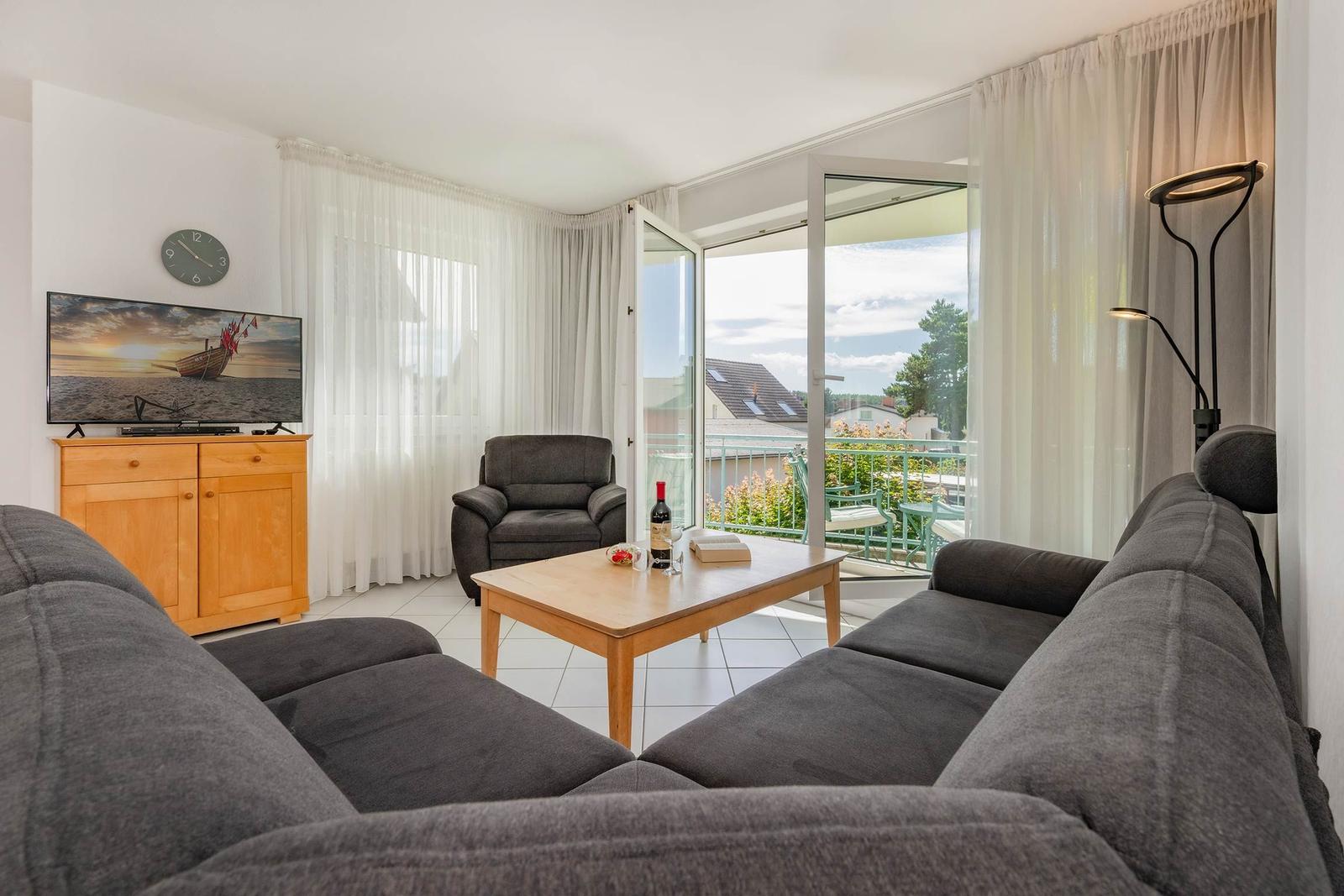 Wohnzimmer mit Sofa, Couchtisch und Fernseher. Durchgang zur Terrasse mit Blick auf Dächer.