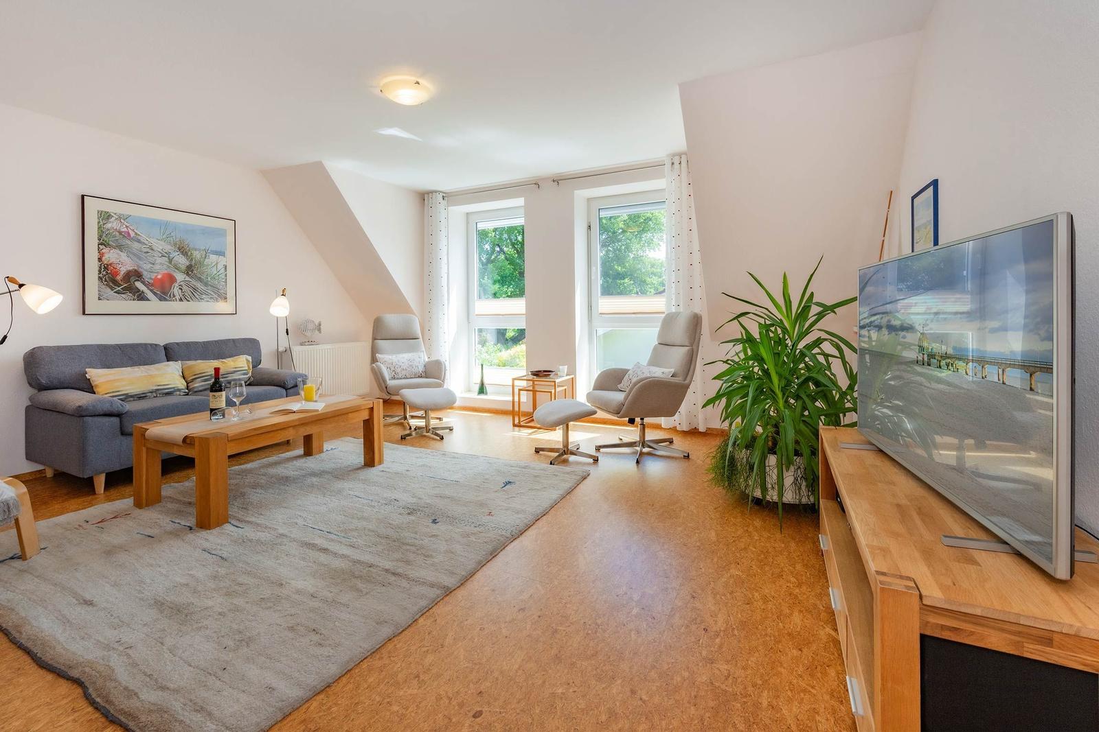 Wohnzimmer mit Sofa, zwei Sesseln, TV und Fenster mit Blick auf Grün.