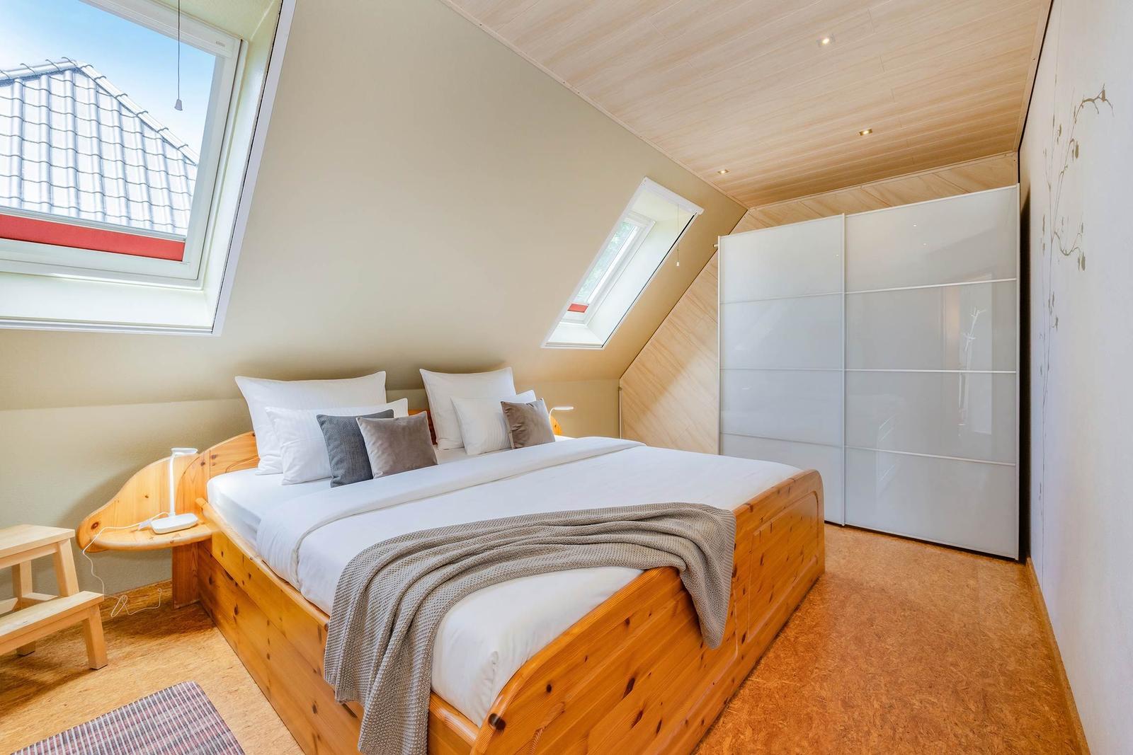 Schlafzimmer mit Doppelbett, Dachschrägen, Fenster und Kleiderschrank.