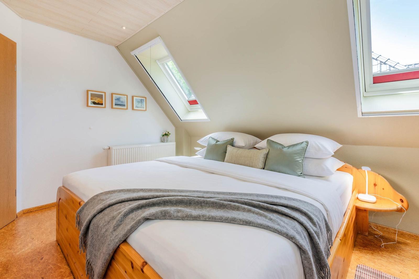 Schlafzimmer mit Holzbett, Dachschrägen und Fenstern.