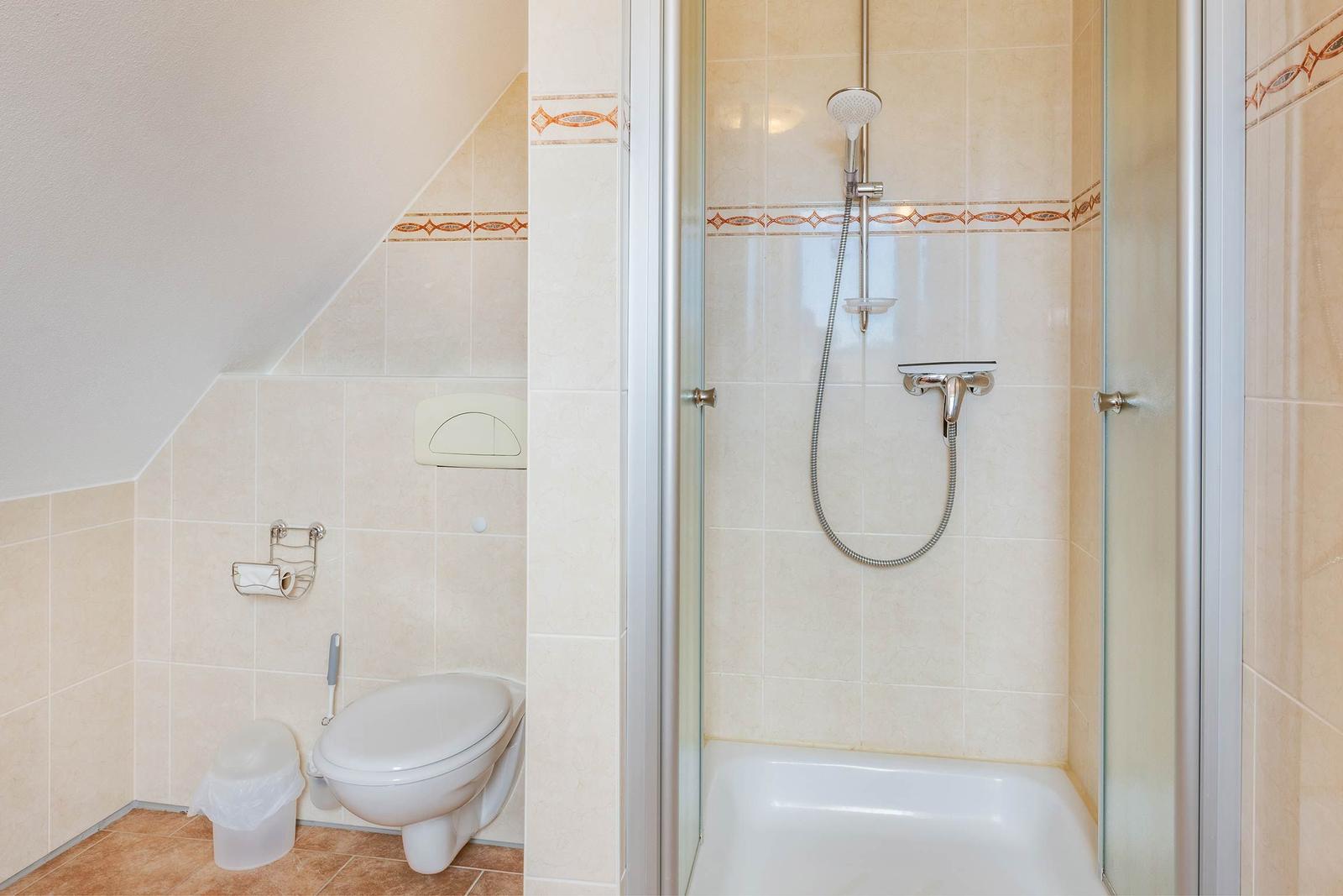 Bad mit Dusche, Toilette und Toilettenpapierhalter an der Wand.
