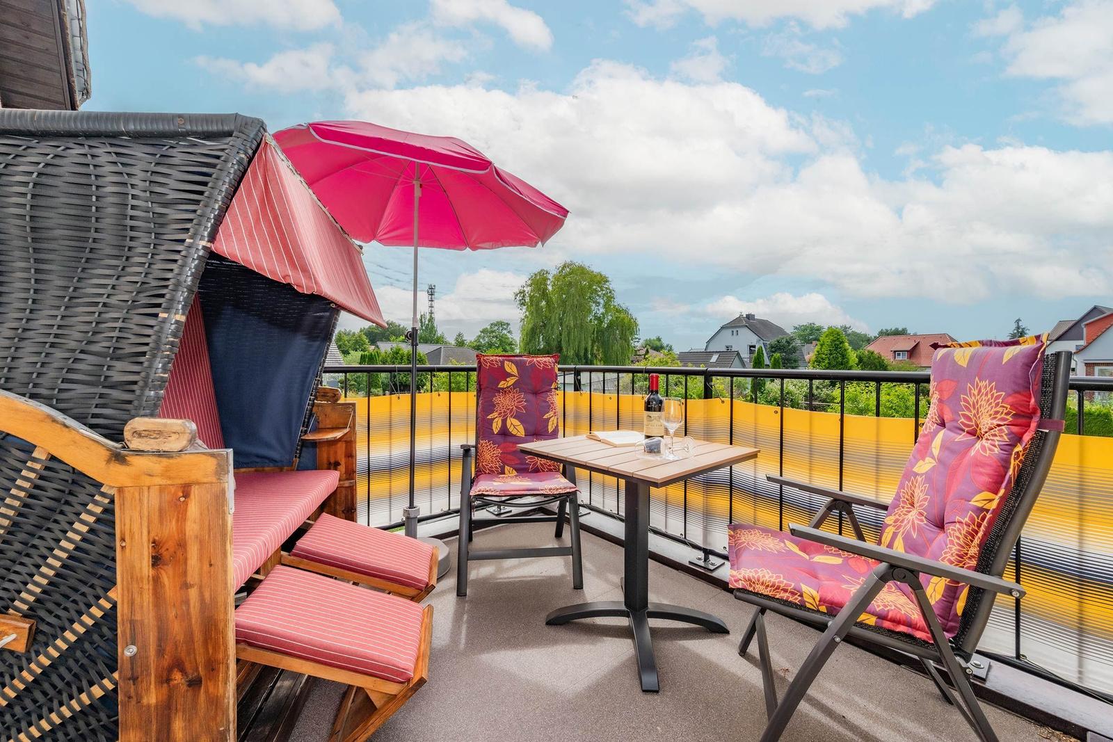 Terrasse mit Sonnenschirm, Tisch und Stühlen. Blick auf Wohngebiet und Bäume.