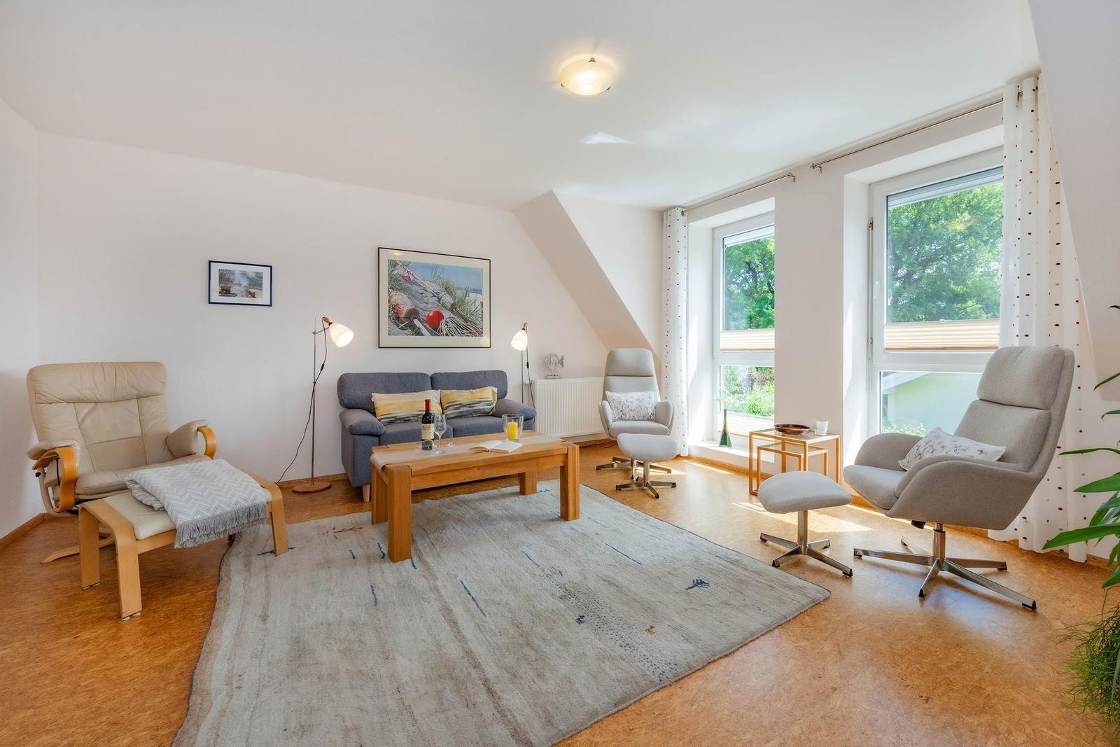 Wohnzimmer mit Sofa, Sesseln und Fenstern. Holzfußboden und Teppichboden.