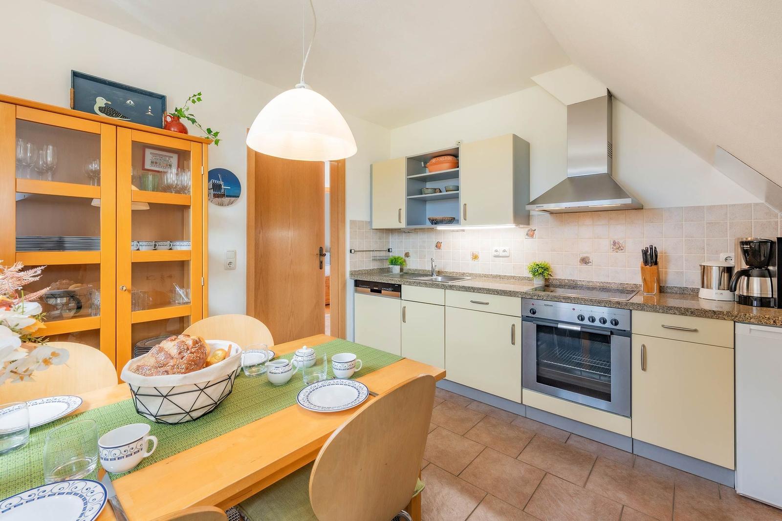 Küche mit Essbereich, Edelstahlherd und Holztisch mit Geschirr.