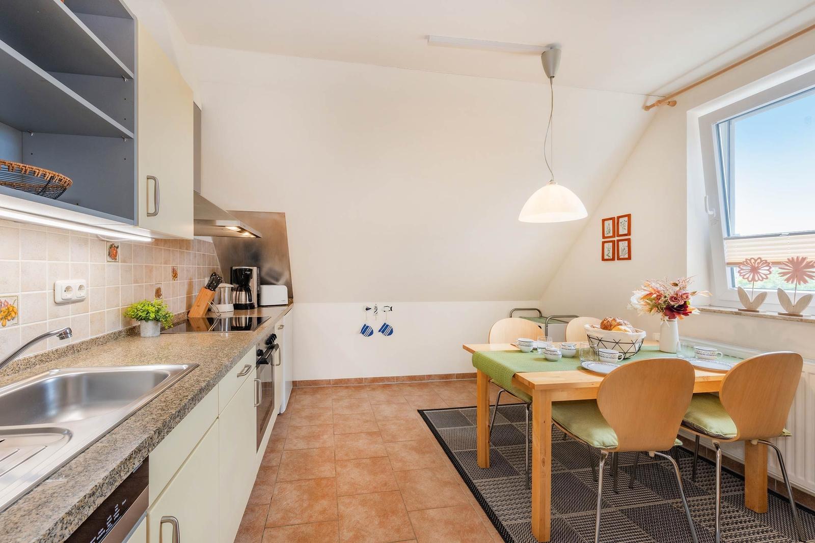 Küche mit Essbereich, Holztisch, Stühle und Fenster mit Blumen.