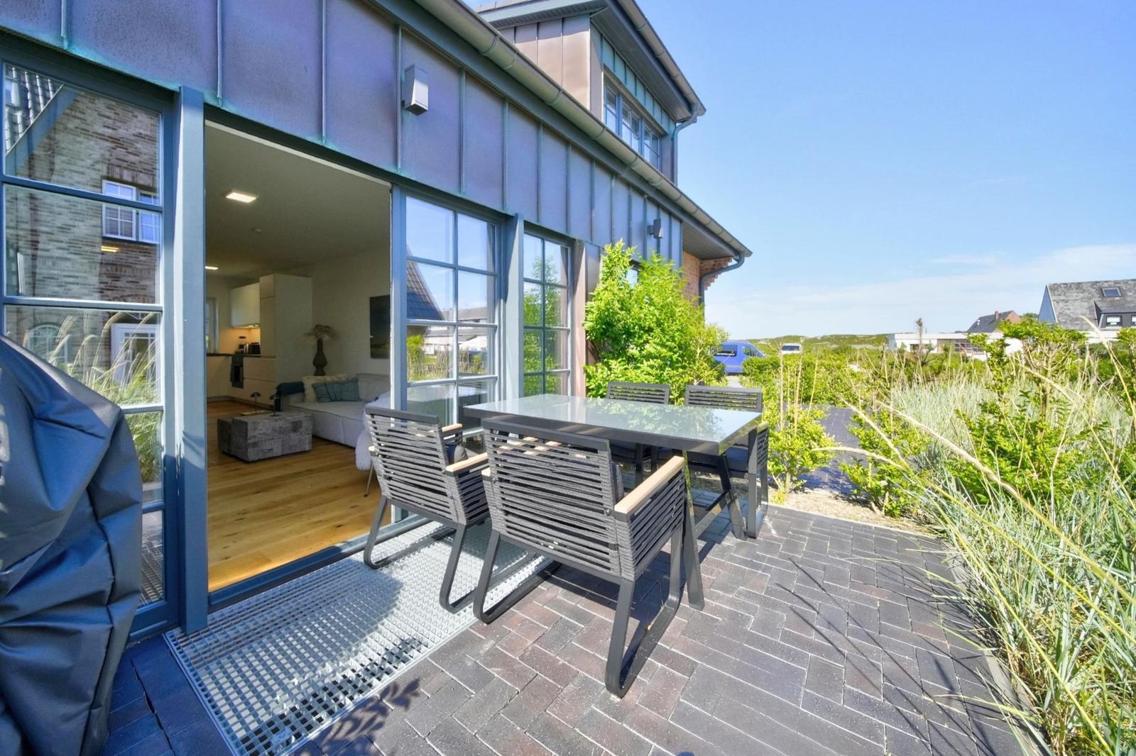 Terrasse mit Tisch und Stühlen, Blick ins Wohnzimmer mit Holzboden und Sofa.