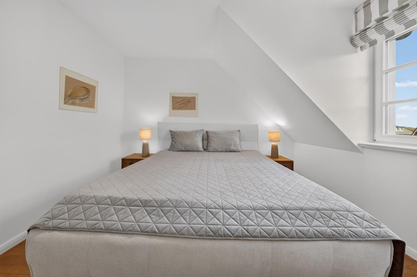 Schlafzimmer mit Dachschräge, Bett, Nachttischen und Fenster.